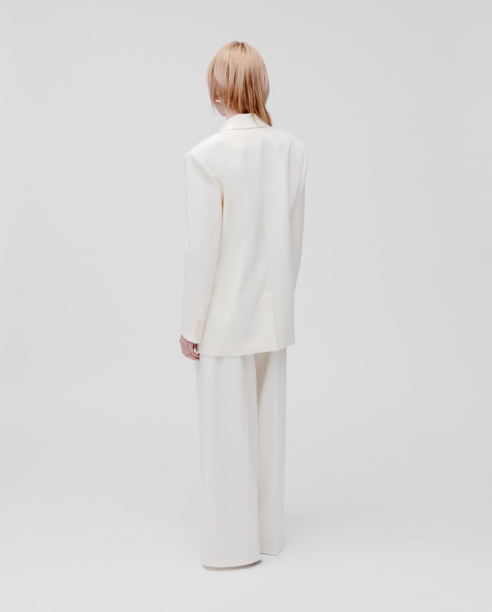 A person with light hair wears the IVY OAK JUDITH Blazer, a relaxed-fit, double-breasted white suit, standing with their back to a plain white background.