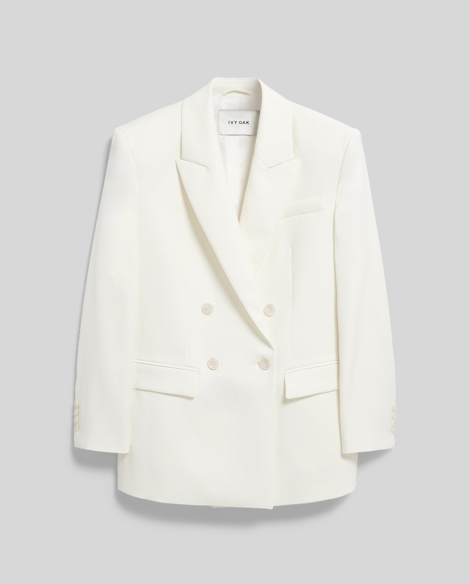 The IVY OAK JUDITH Blazer is a white, lightweight wool-blend double-breasted jacket with notched lapels and front pockets, shown against a light grey background.