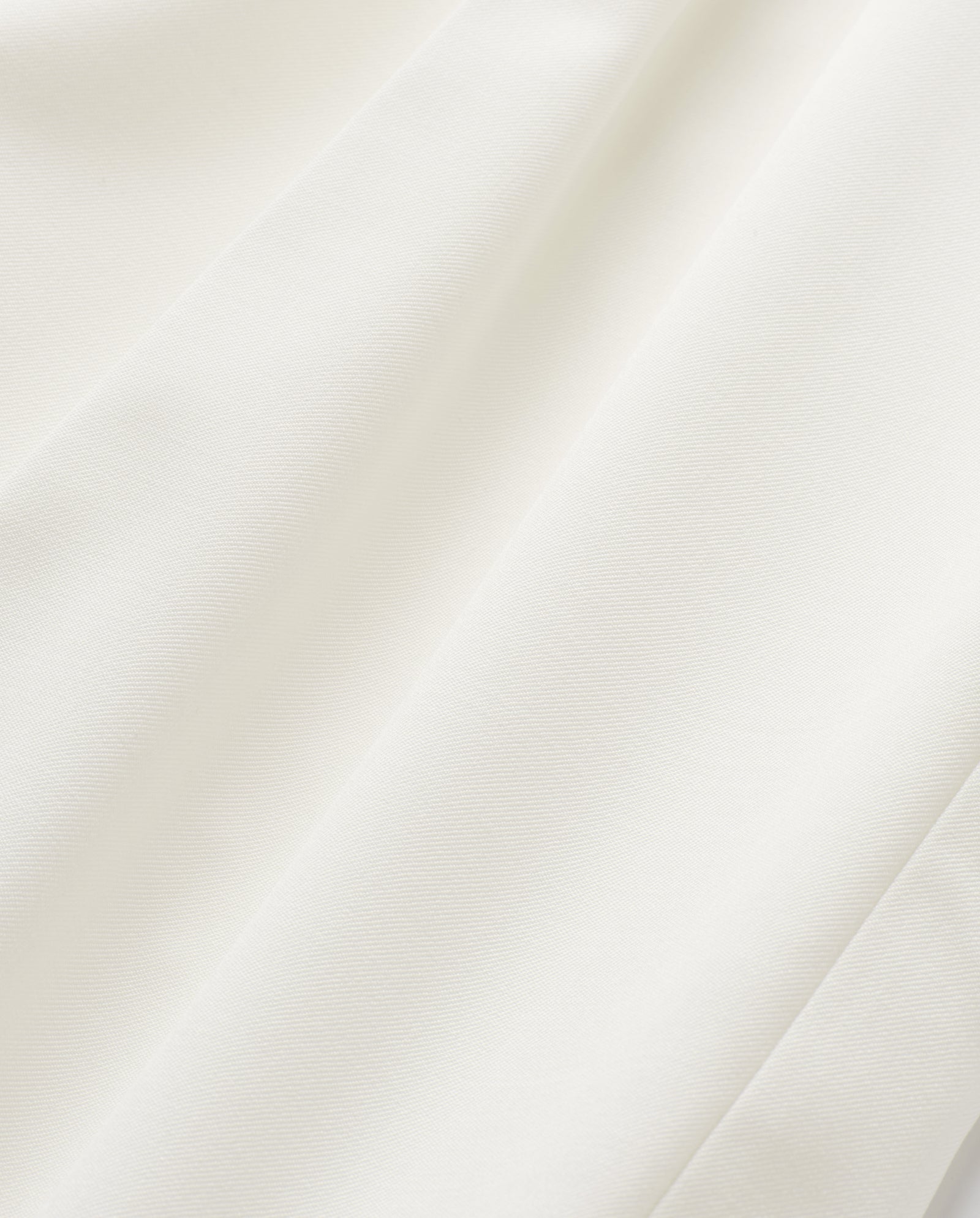 The JUDITH Blazer by IVY OAK features a white, lightweight wool-blend fabric with soft folds that create gentle shadows and a smooth, textured surface.