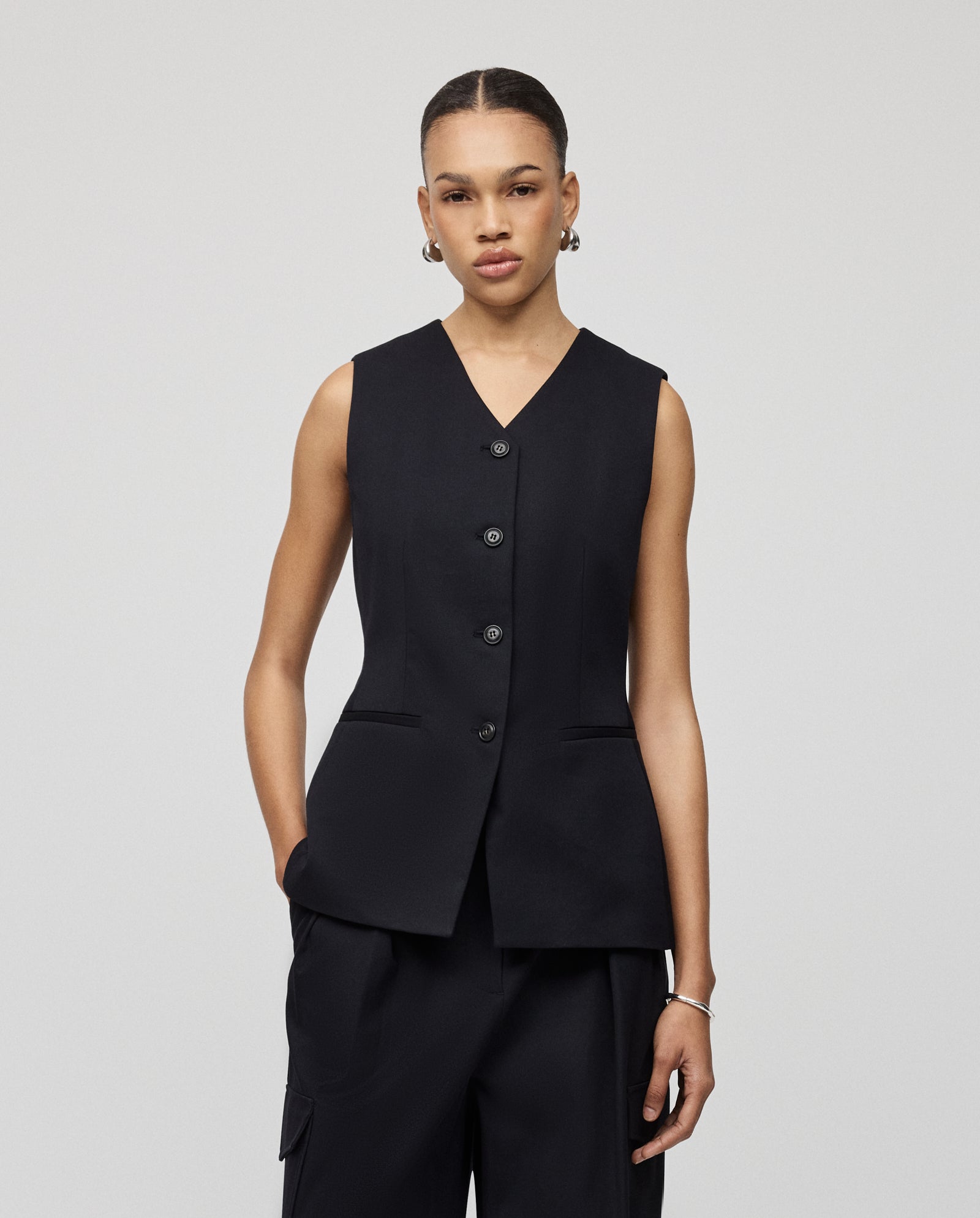 A woman wears the IVY OAK JUNIPER ROSE sleeveless black body silhouette vest paired with matching black pants, standing against a plain background.