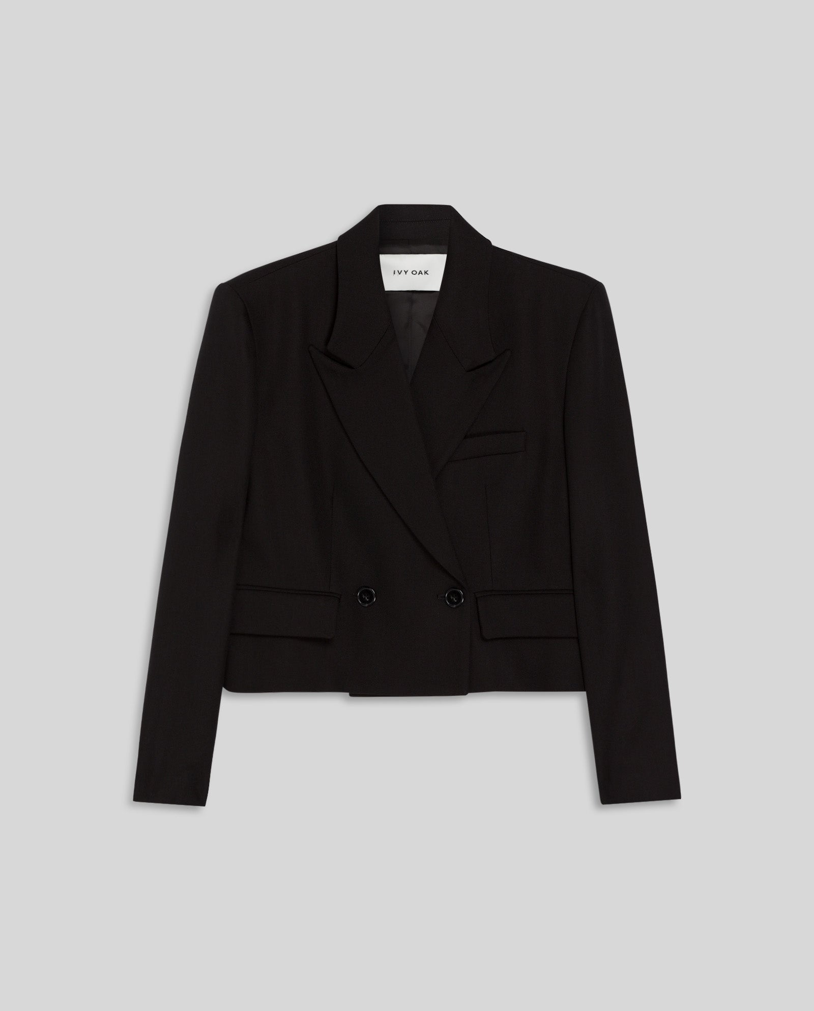 The IVY OAK JENNY ANN Blazer is a black cropped double-breasted blazer with lapels and flap pockets, featuring a boxy fit and structured tailoring, shown on a light gray background.