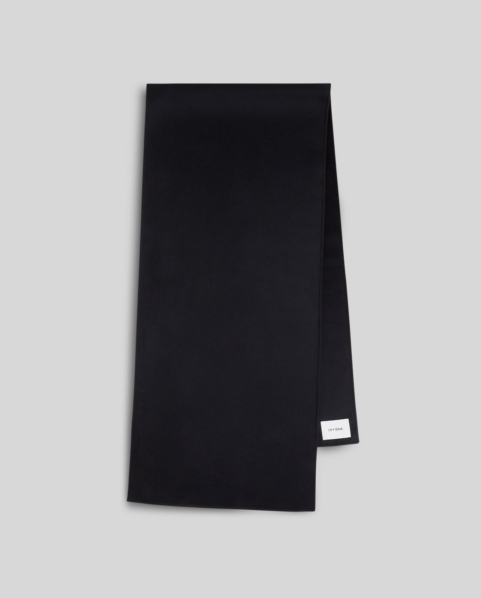 A cozy AMY Scarf by IVY OAK in plain black with a small white label, shown on a light gray background.