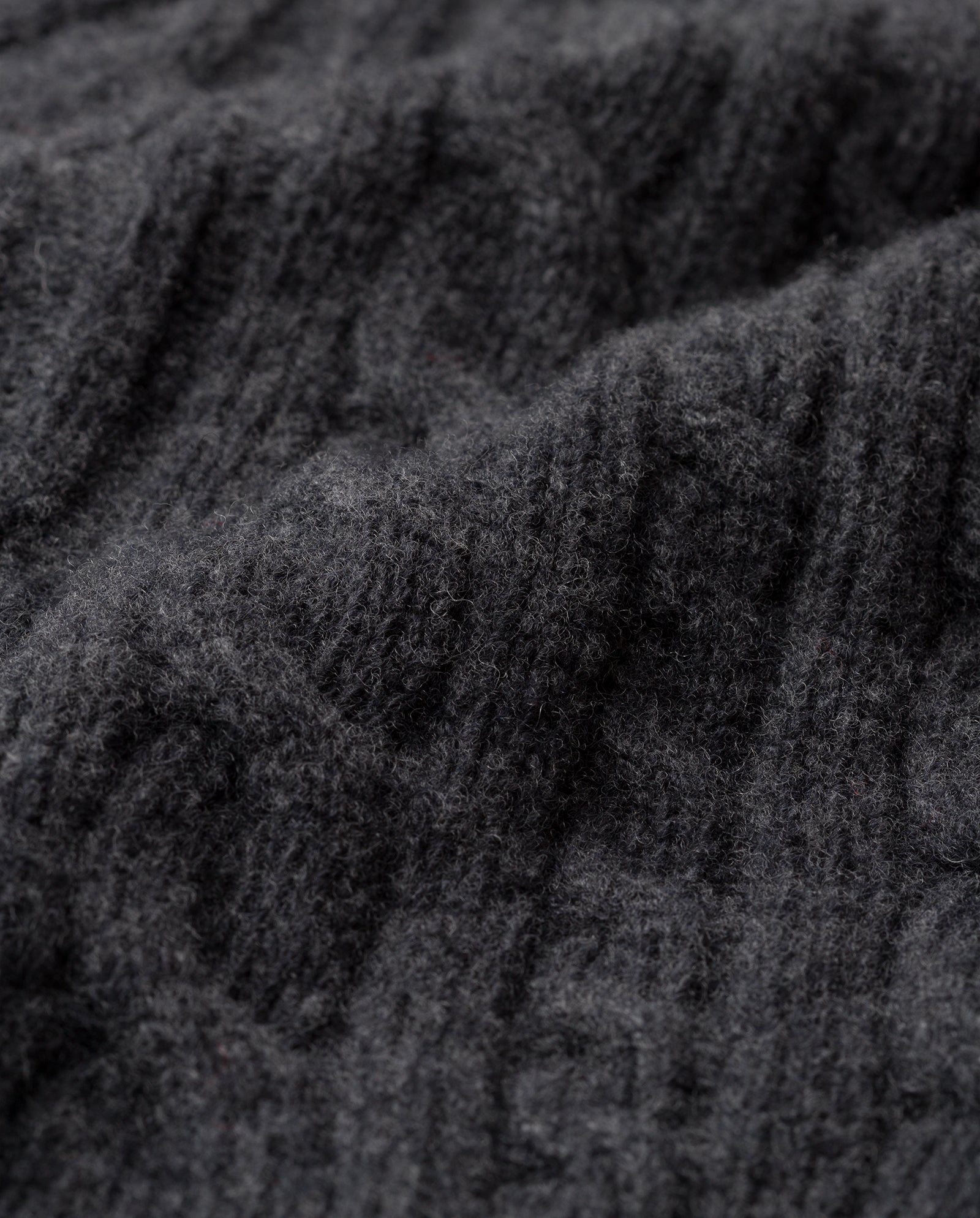 Close-up of dark gray, textured knit fabric with a subtle cable pattern—the AMELIA Scarf by IVY OAK, crafted from luxurious supergeelong extrafine merino wool, is perfect for cozy winter days.
