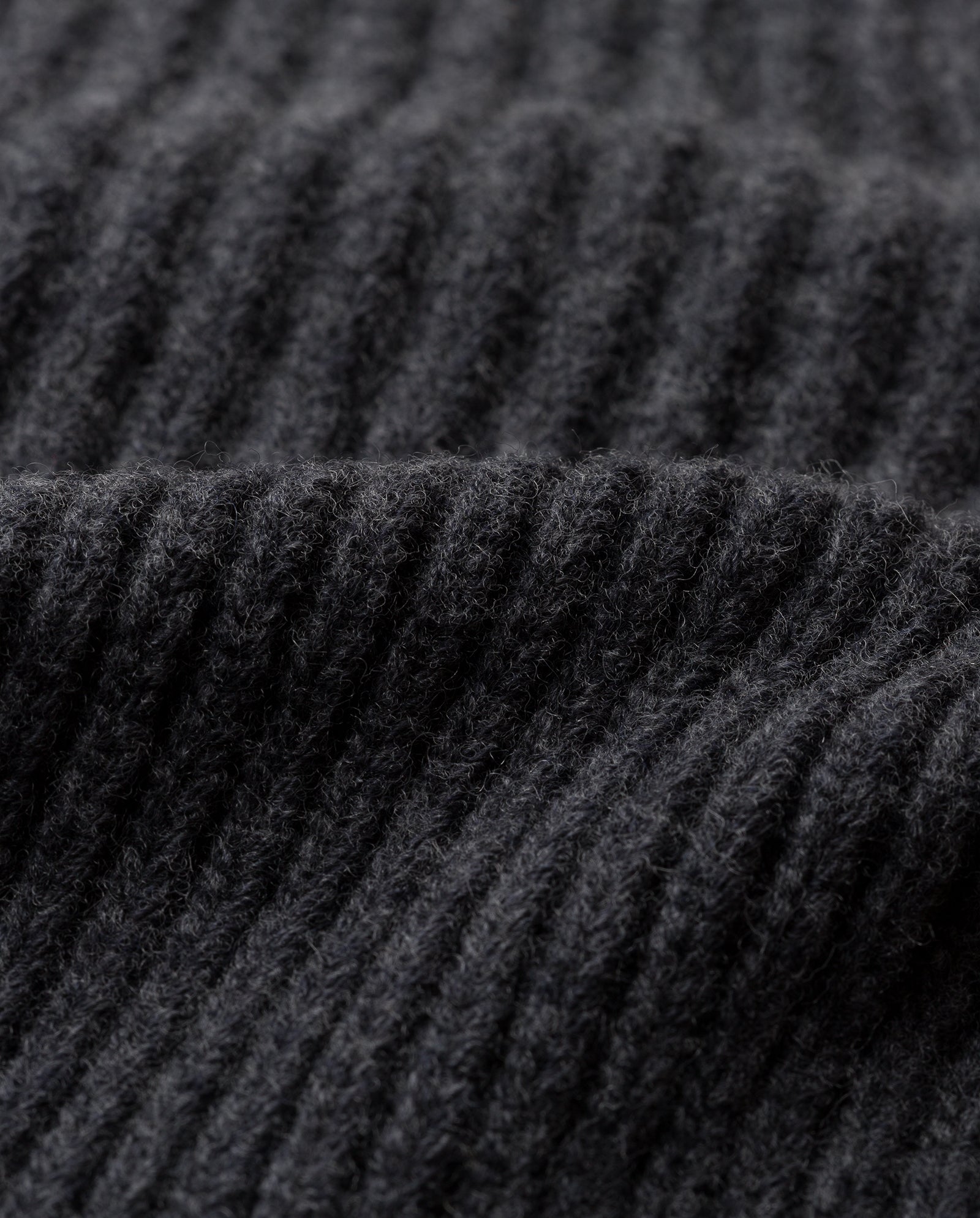 Close-up of the AMBER Beanie by IVY OAK, featuring black ribbed knit fabric made from supergeelong extrafine merino wool, highlighting its soft and textured surface.