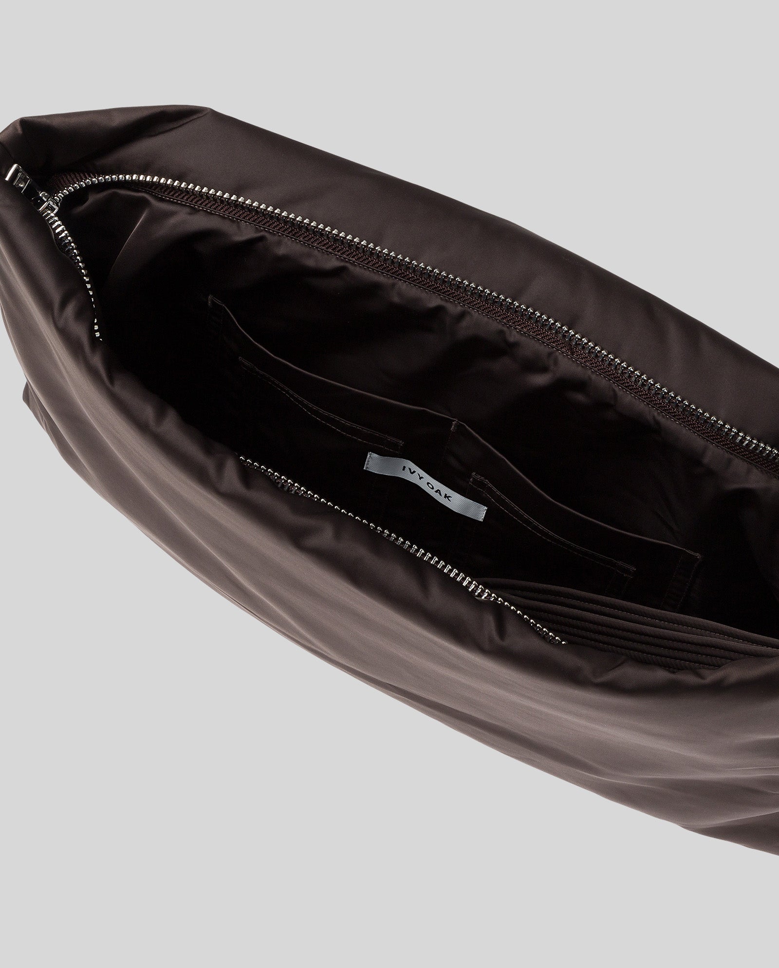 Open the AMINA ROSE Clutch by IVY OAK in dark brown padded shiny material, featuring a metal zip, visible inner pocket, and an inner label marked IVY OAK.