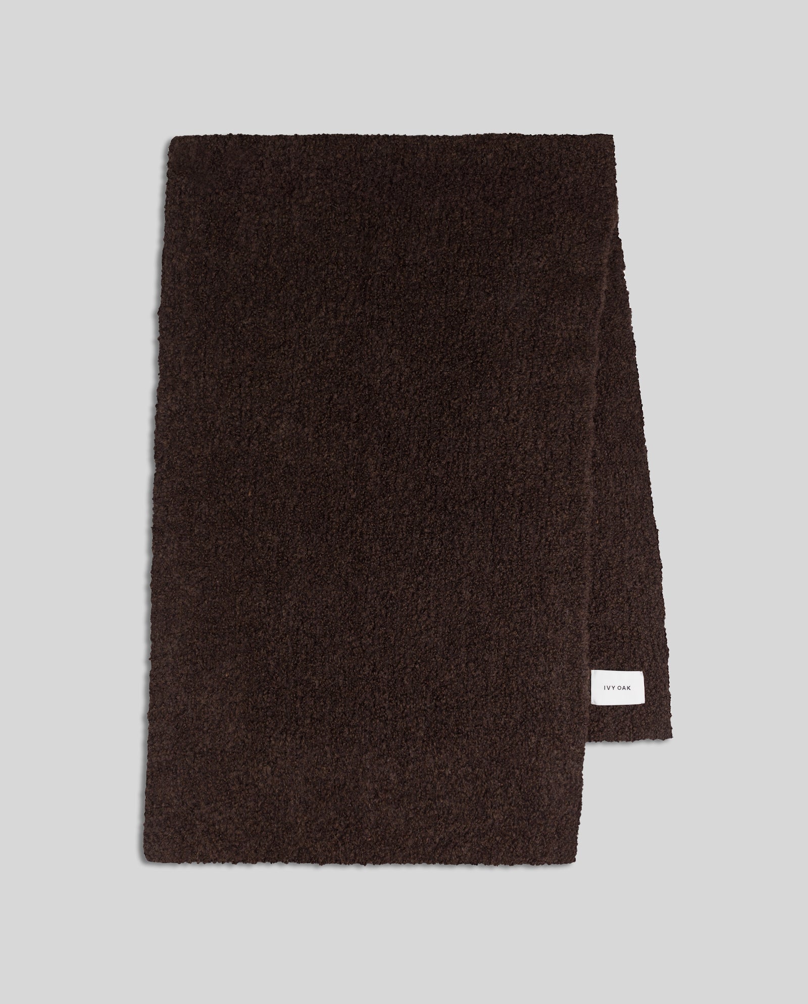 The ALINA Scarf by IVY OAK is a dark brown, textured bouclé wool scarf with a small white label on the lower edge—a cozy winter essential.
