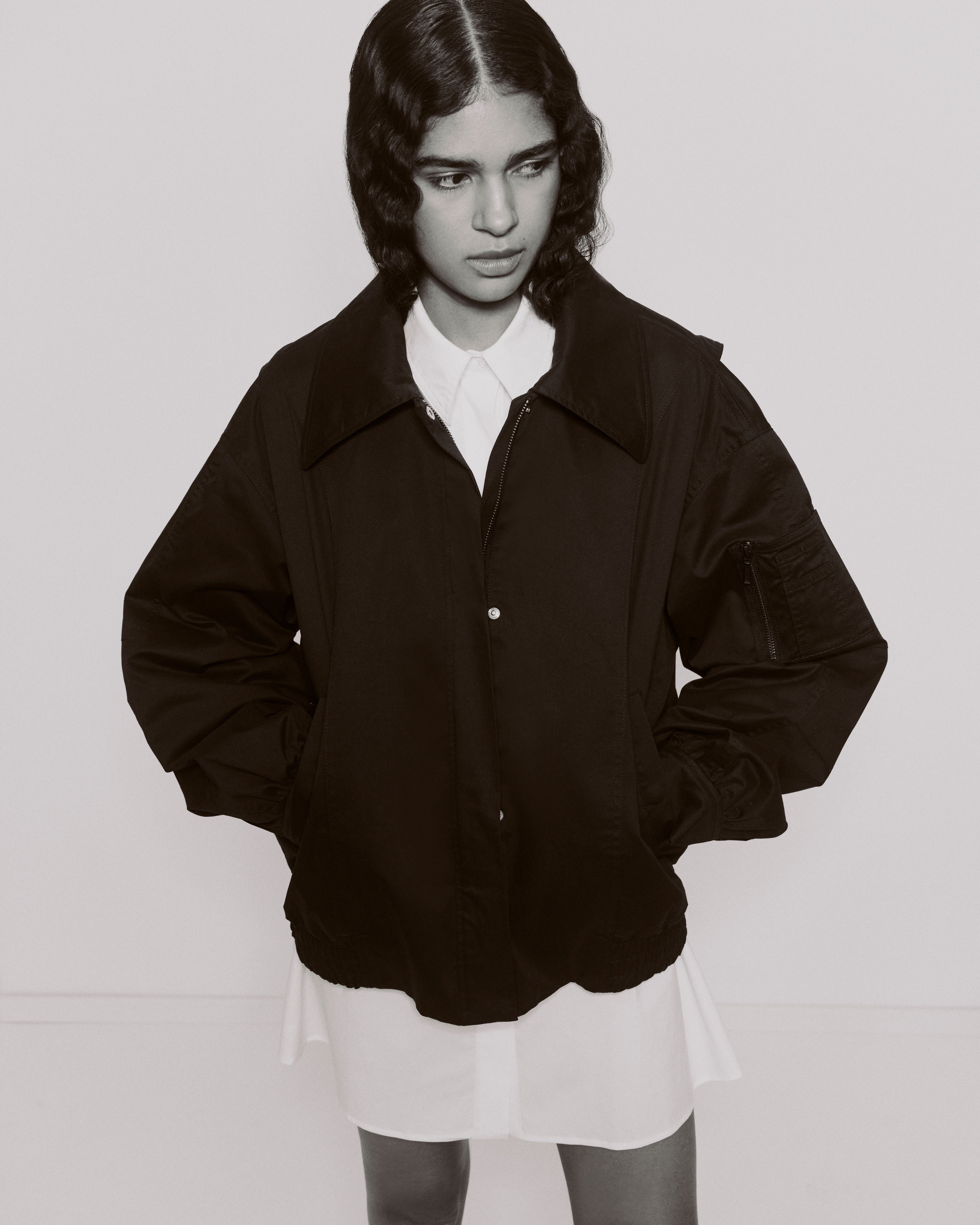 black and white image of a young woman in a long white shirt and a black jacket.