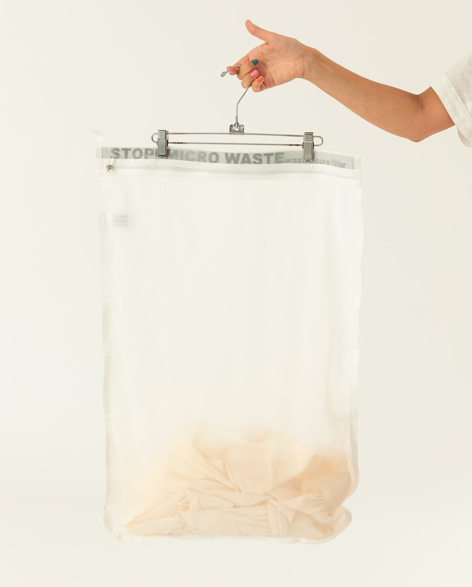 A hand holds a hanger with the IVY OAK GuppyFriend Washbag, a durable bright white polyamide mesh laundry bag designed to stop micro waste.