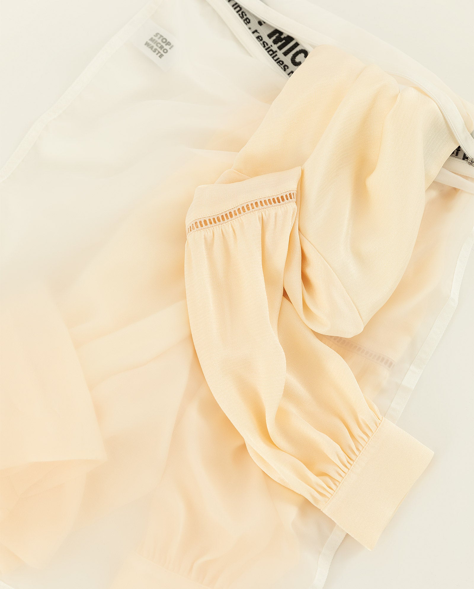 The IVY OAK GuppyFriend Washbag holds a sheer beige blouse with gathered sleeves, made from soft polyamid—ideal for protecting delicate items while washing.