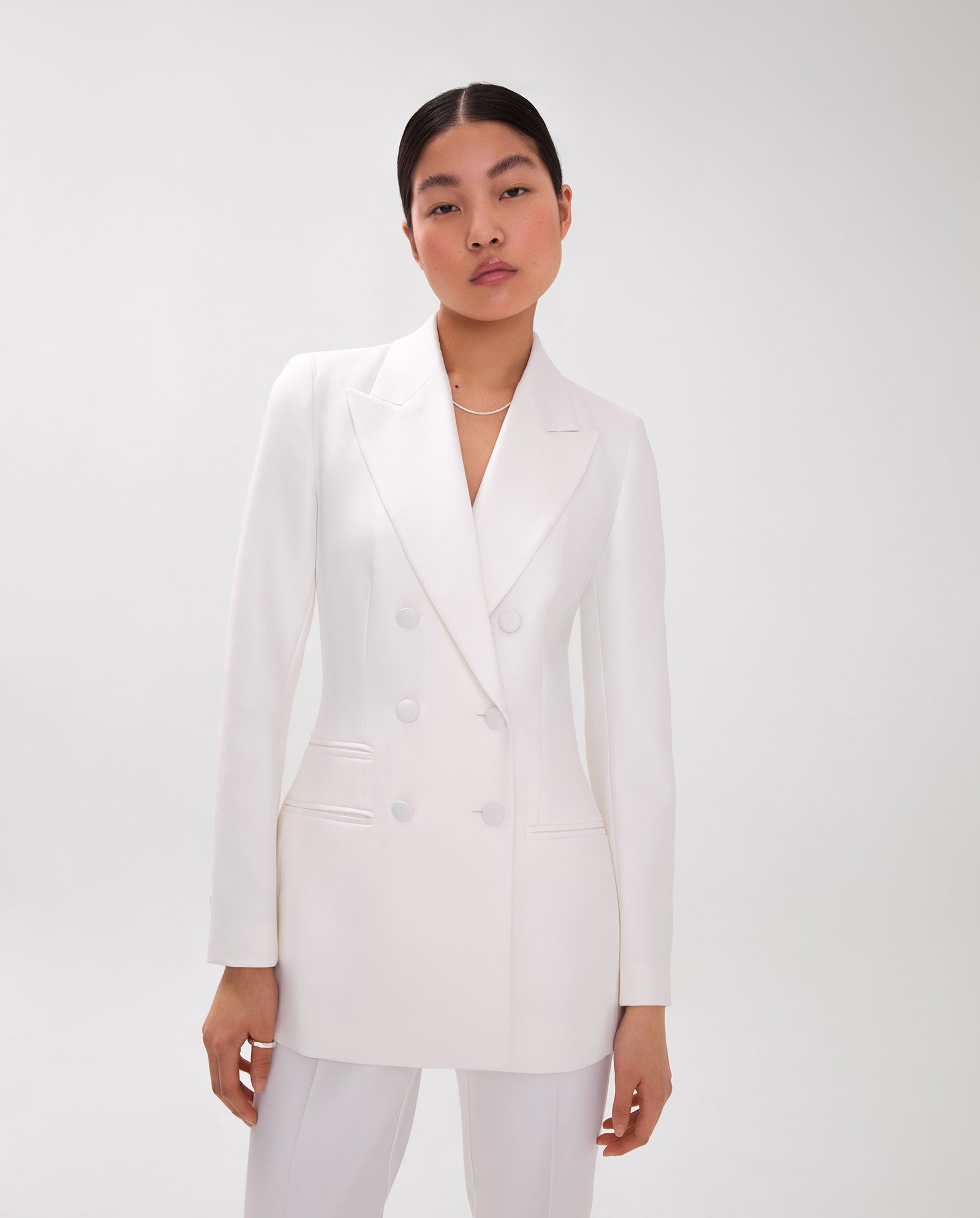 A woman wears the IVY OAK JENNIFER Blazer, a white double-breasted style with wide lapel collar and matching pants, standing against a plain white background.