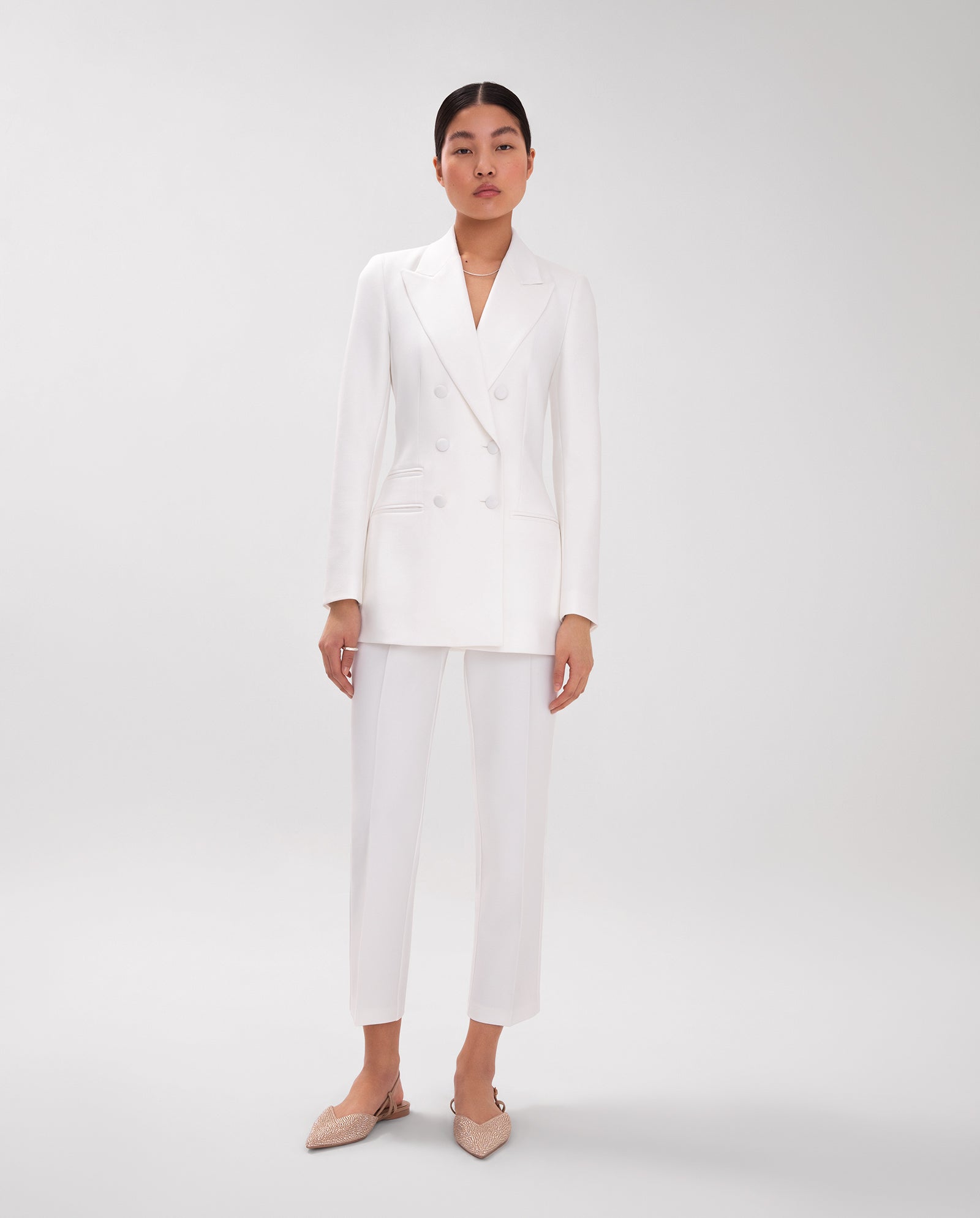 A woman wears the IVY OAK JENNIFER Blazer, a white double-breasted suit with wide lapel collar and cropped pants, standing against a plain background.