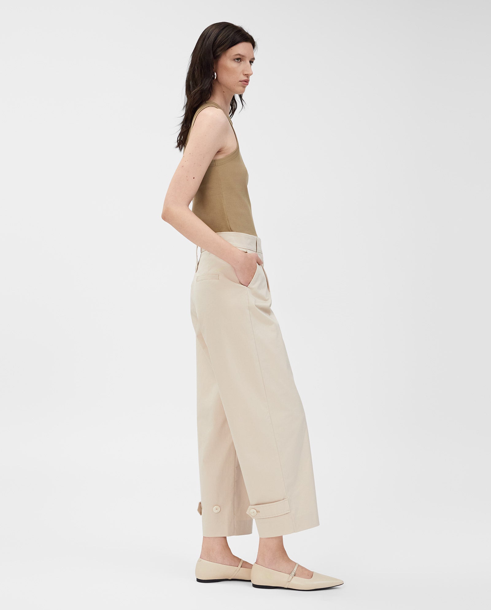 A woman stands in profile against a plain white background, wearing the IVY OAK KLARA ANN Tanktop in beige and cream wide-leg pants.