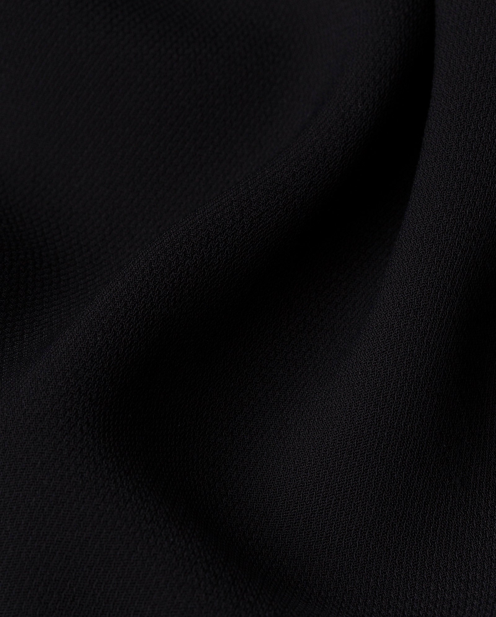 Close-up of black textured fabric with soft folds and subtle shadows, suggesting the stylish PAULINA Jumpsuit by IVY OAK with its defined waistband.