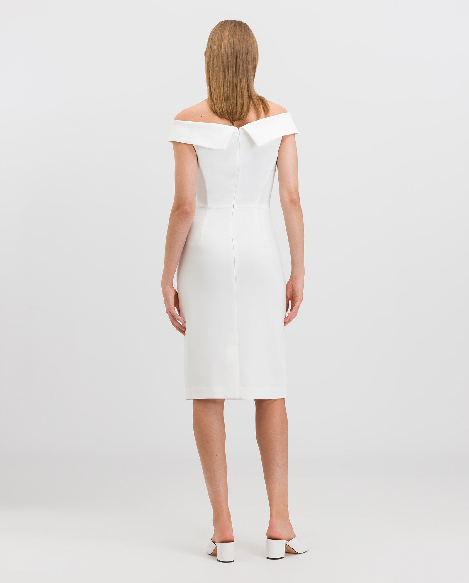 A woman wearing the IVY OAK MAREN Dress with a schulterfrei Carmen-Ausschnitt and körpernaher Passform, paired with white heels, stands facing away against a plain light background.