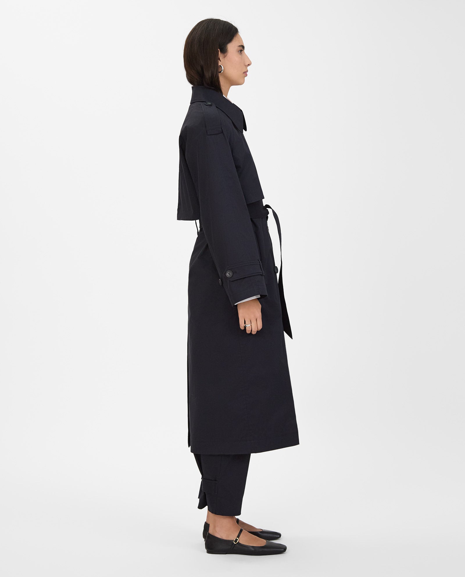Woman in the IVY OAK CORALINE oversized black double breasted trenchcoat, paired with black pants and flats, standing in profile against a white background.
