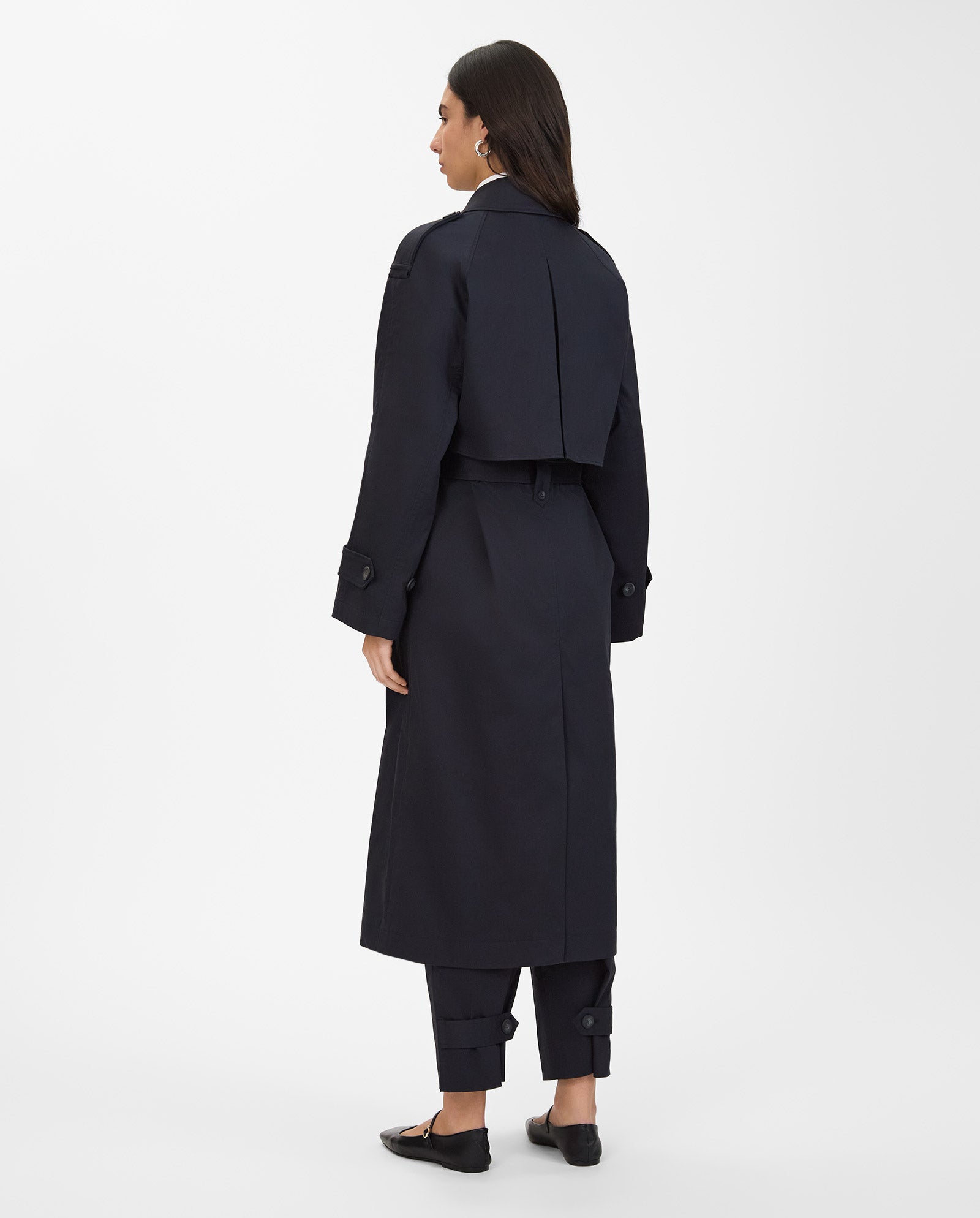 A woman stands facing away from the camera, wearing the IVY OAK CORALINE Coat—an oversized, double-breasted trenchcoat made from organic cotton—with matching pants.
