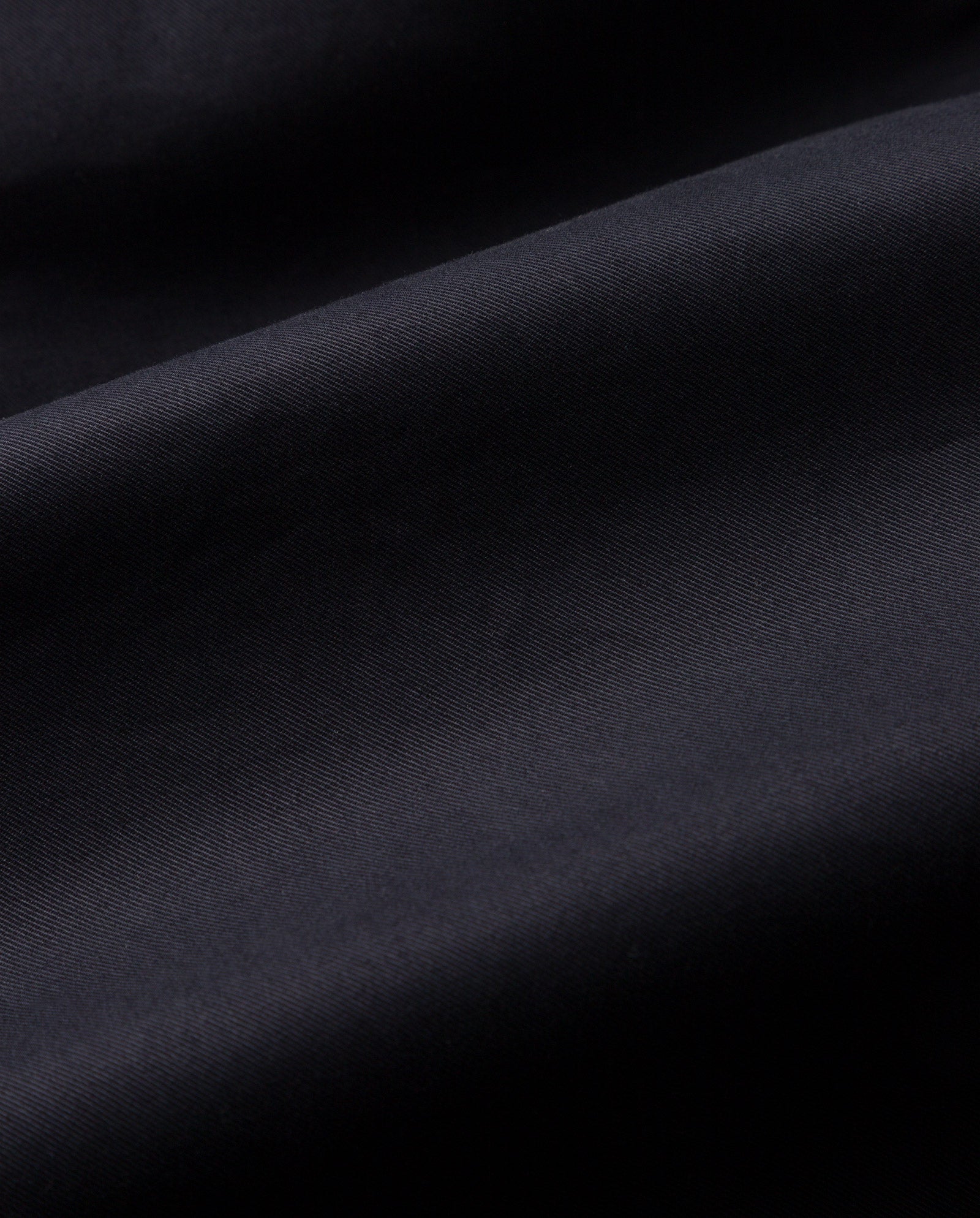 Close-up of the IVY OAK CORALINE Coat’s smooth black organic cotton fabric, featuring gentle folds and a soft matte texture.