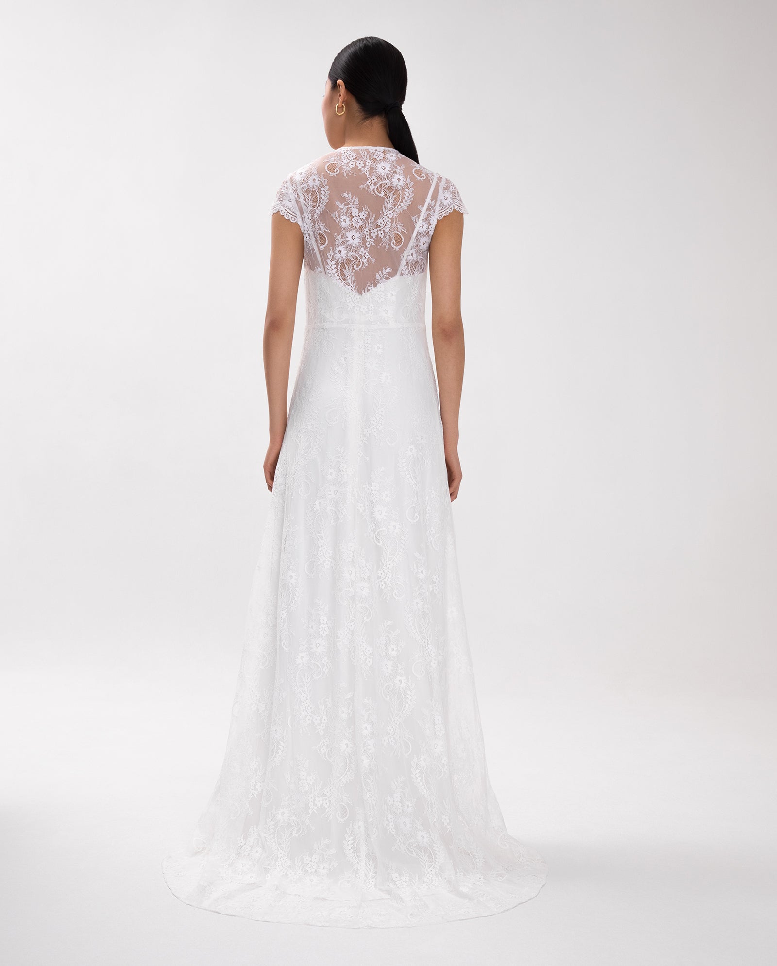 Woman in the IVY OAK DANIELLA ROSE Bridal Dress featuring white lace cap sleeves and an elegant eyelash neckline, shown from the back against a plain background.