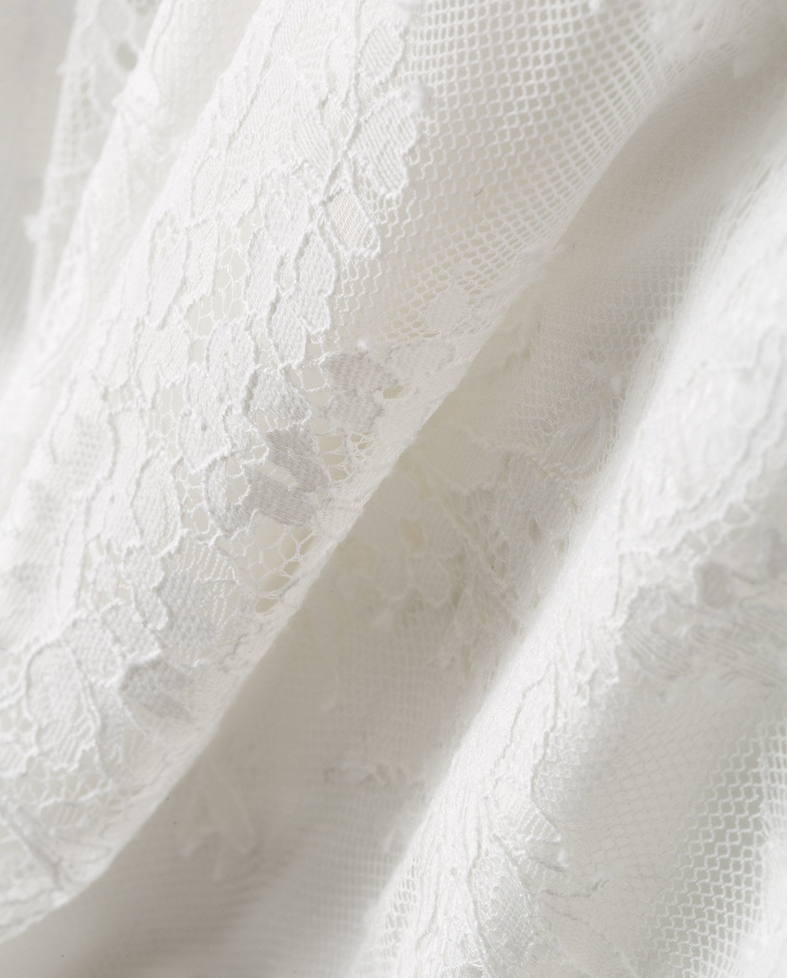 Close-up of DALIA Lace Dress by IVY OAK, featuring white lace fabric with floral patterns and a delicate, sheer texture—ideal for an elegant bridal or wedding look.
