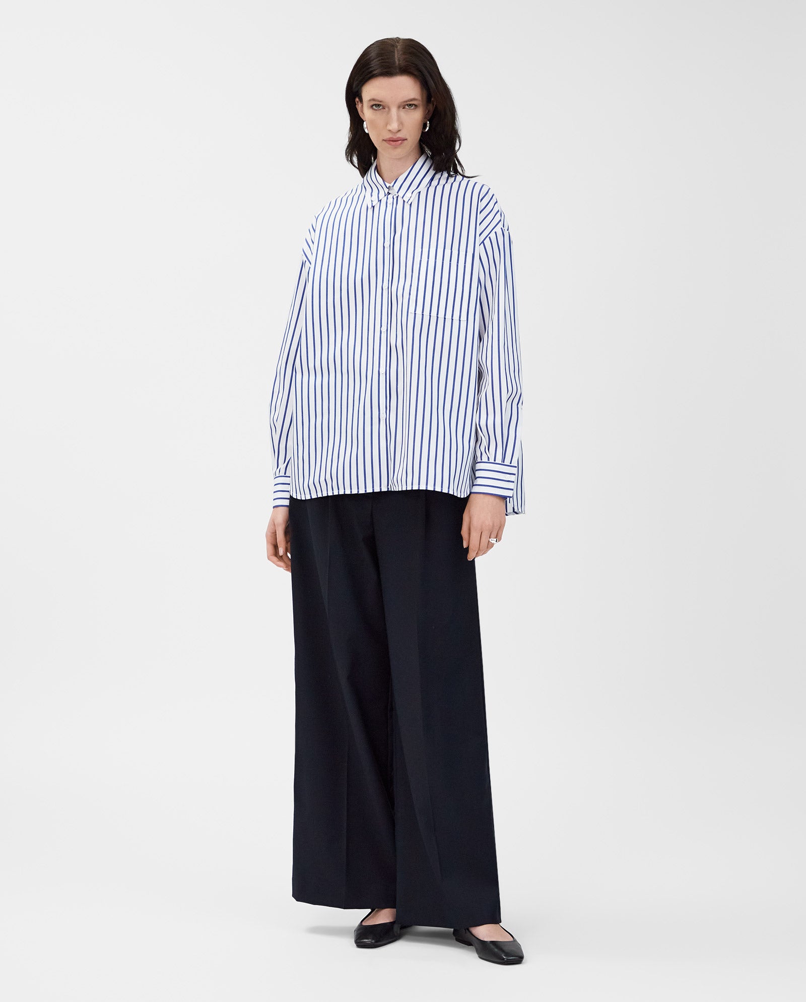 A model wears the IVY OAK BETHANY LILLY Blouse—oversized with a boxy cut and striped cotton pattern—paired with wide black pants and black shoes, standing against a white background.