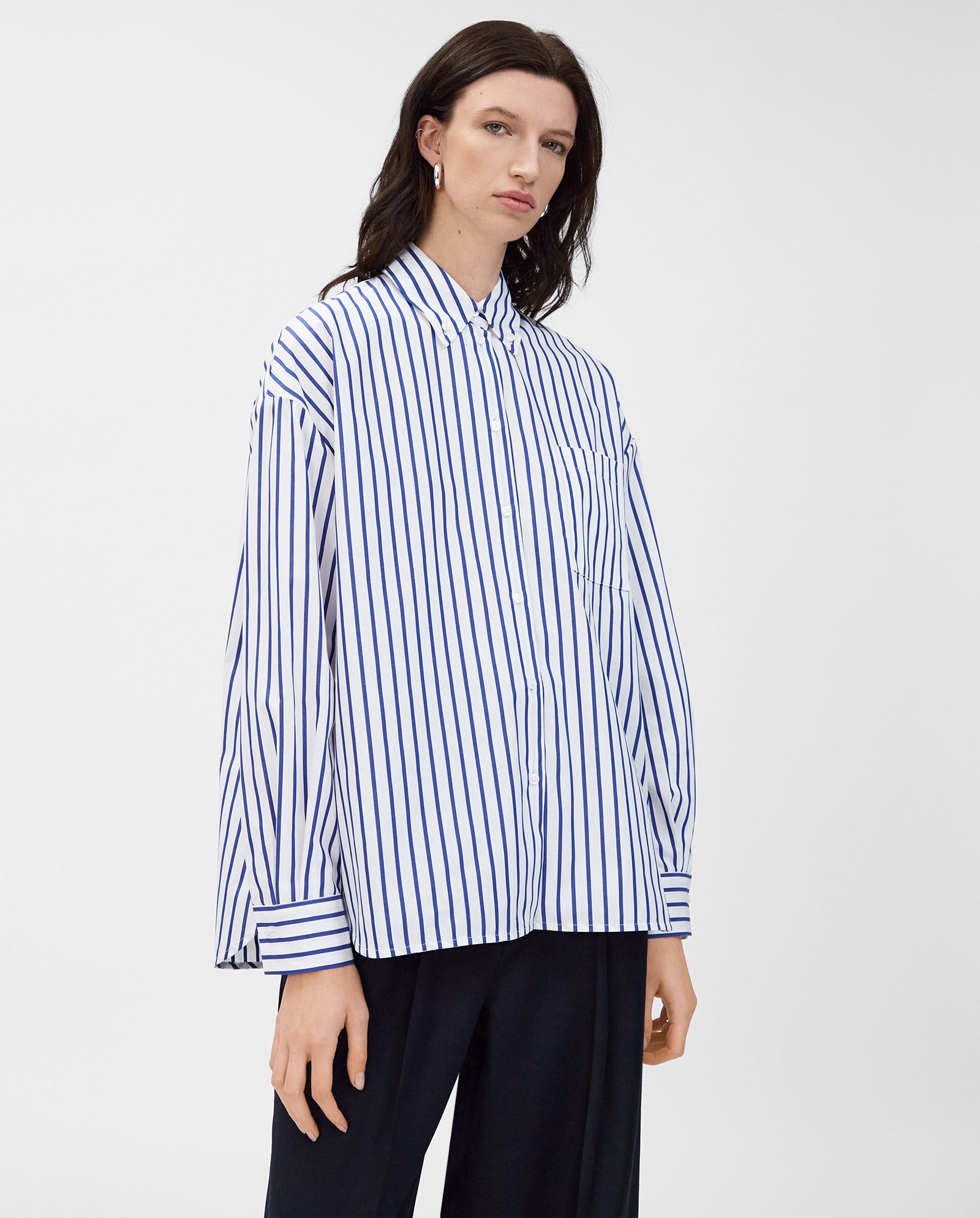 A person wears the IVY OAK BETHANY LILLY Blouse, a loose-fitting blue and white striped cotton top with a boxy cut, paired with black pants against a plain background.