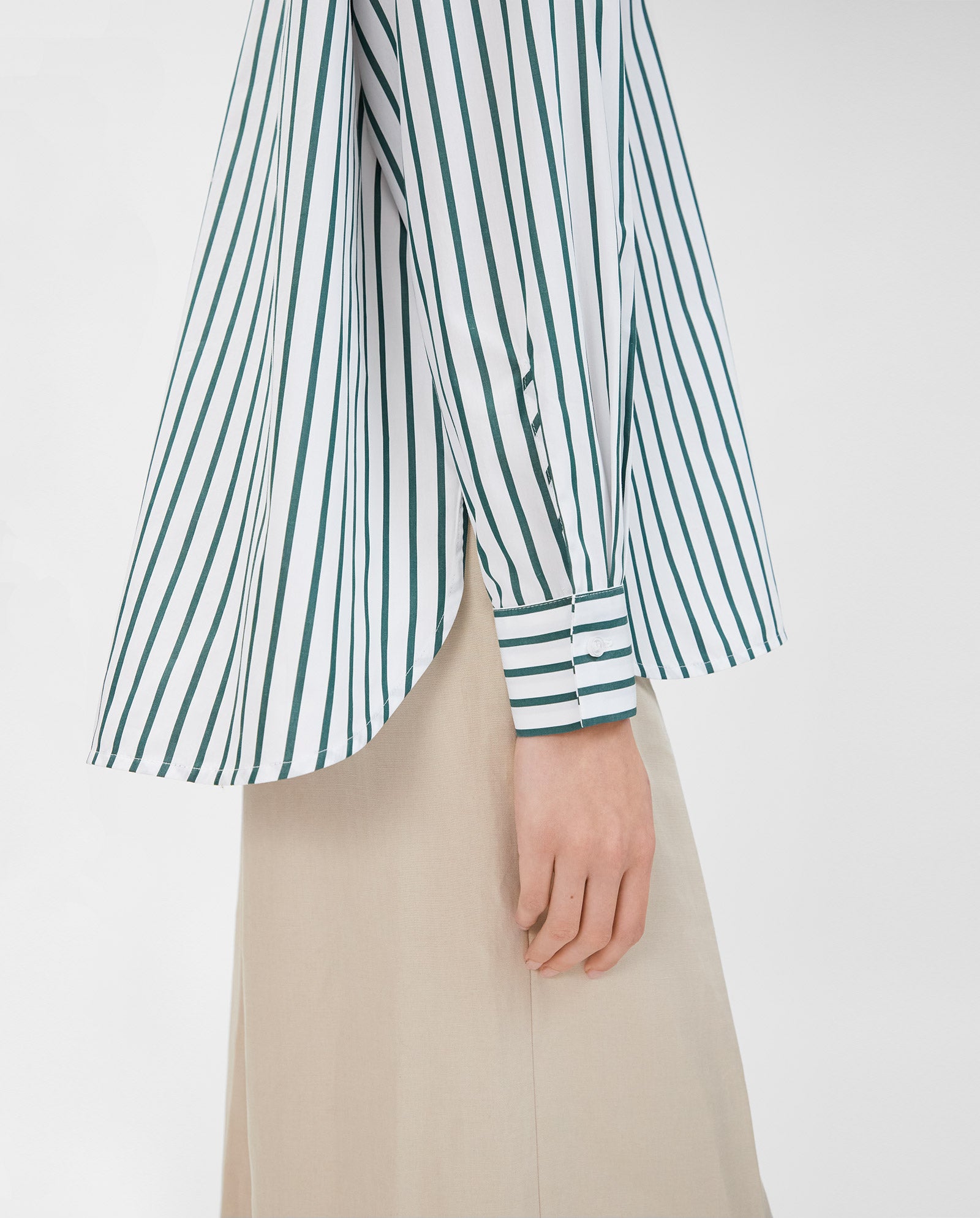 A person is shown from the side wearing the IVY OAK BETHANY LILLY Blouse, featuring green and white stripes, a boxy cut, and cotton fabric, paired with beige pants.
