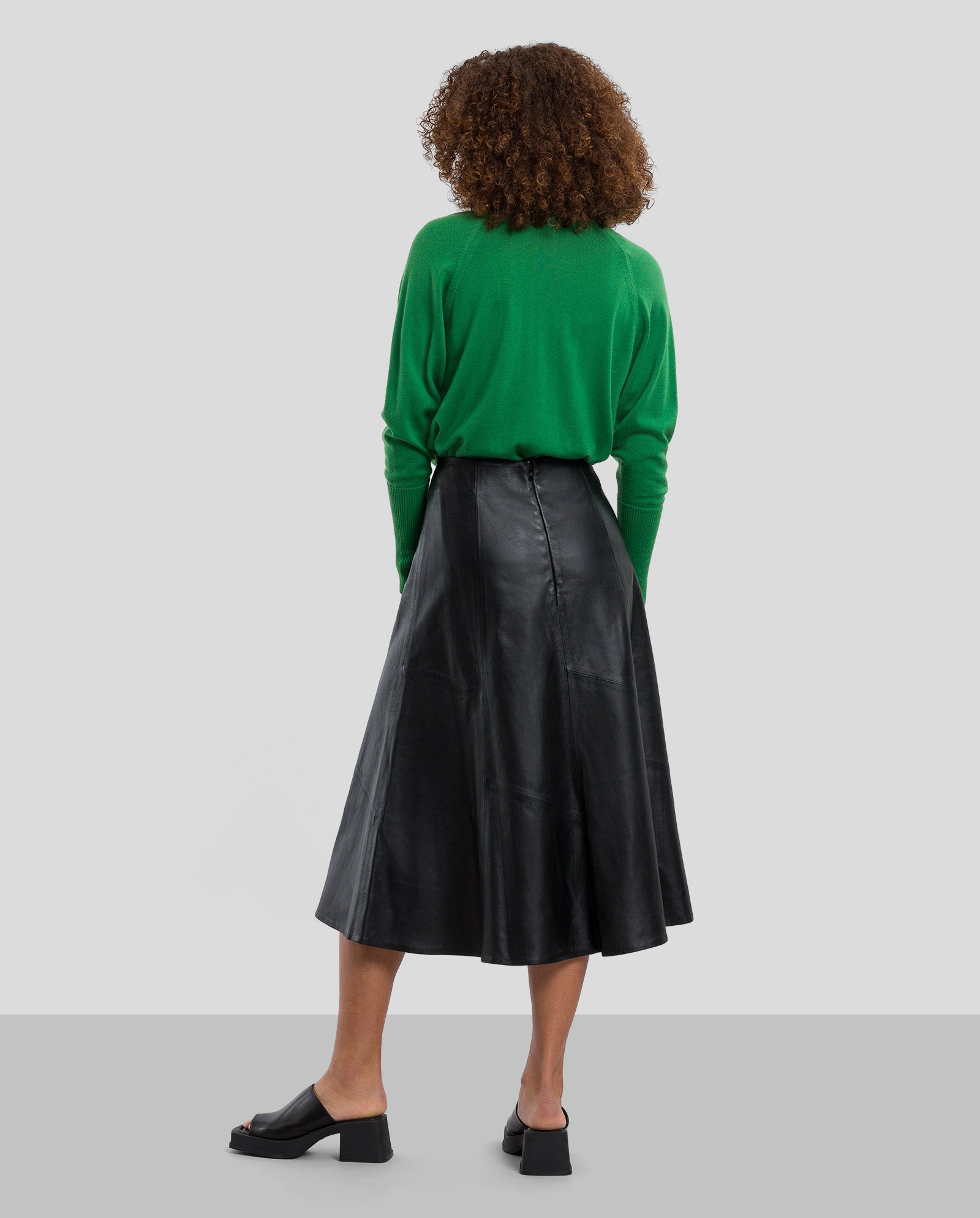 Person with back to camera wearing a green sweater, black sandals, and the IVY OAK LAUREEN Leather Skirt.