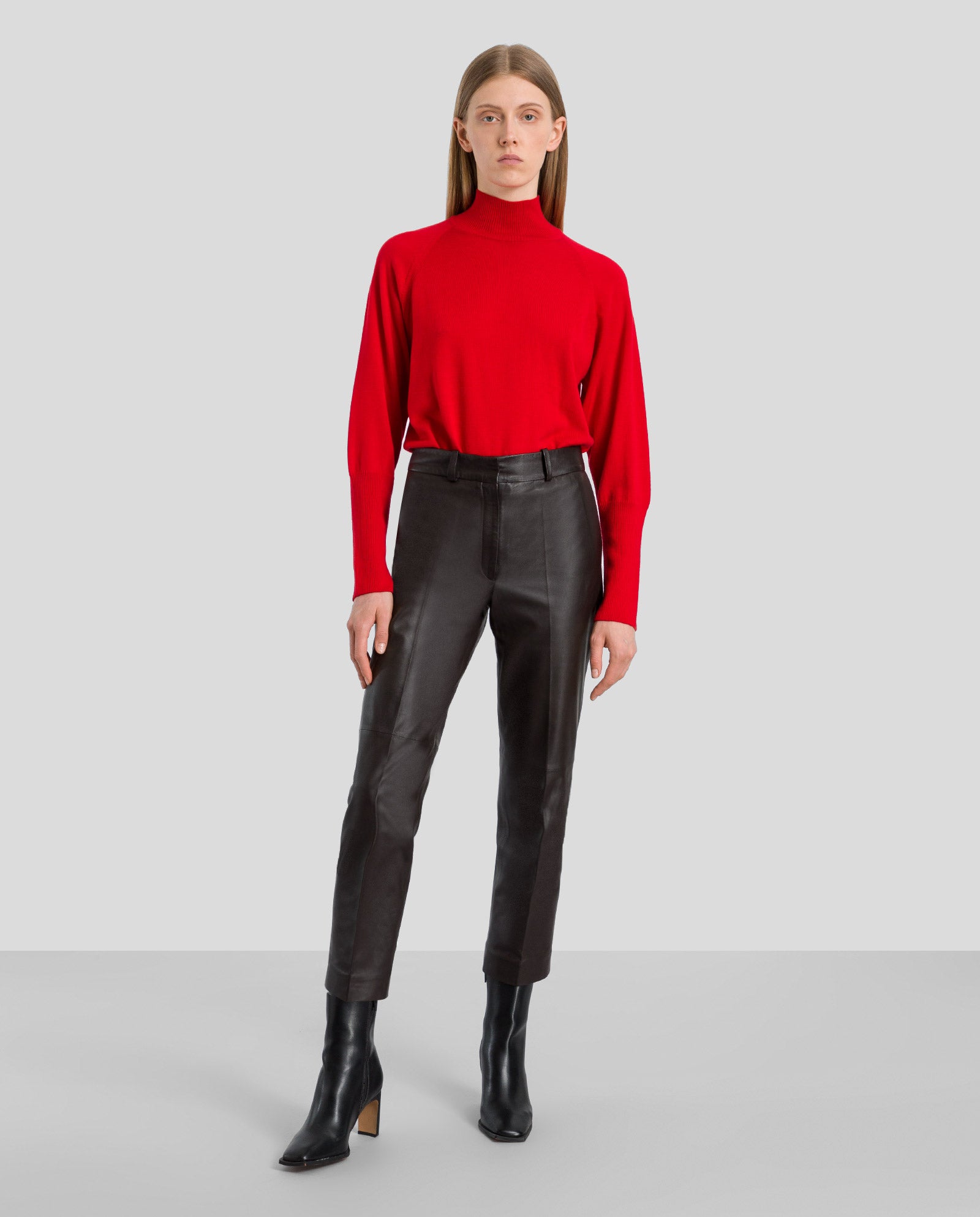 A woman in a red turtleneck sweater styles the IVY OAK LAURA Leather Trousers with black ankle boots, standing against a plain background.