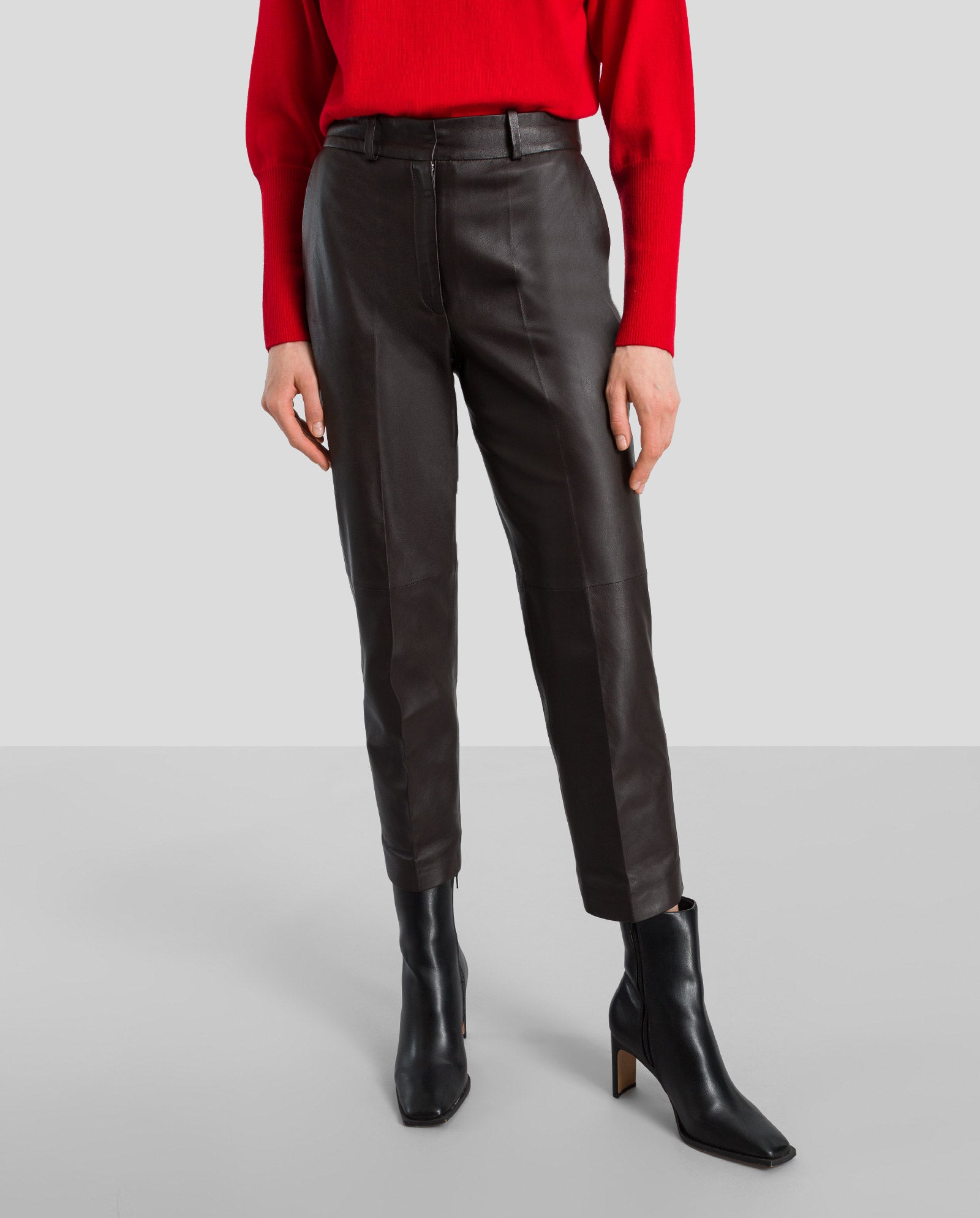 Model wears IVY OAK’s LAURA Leather Trousers with a red sweater and black heeled boots, standing against a plain background.