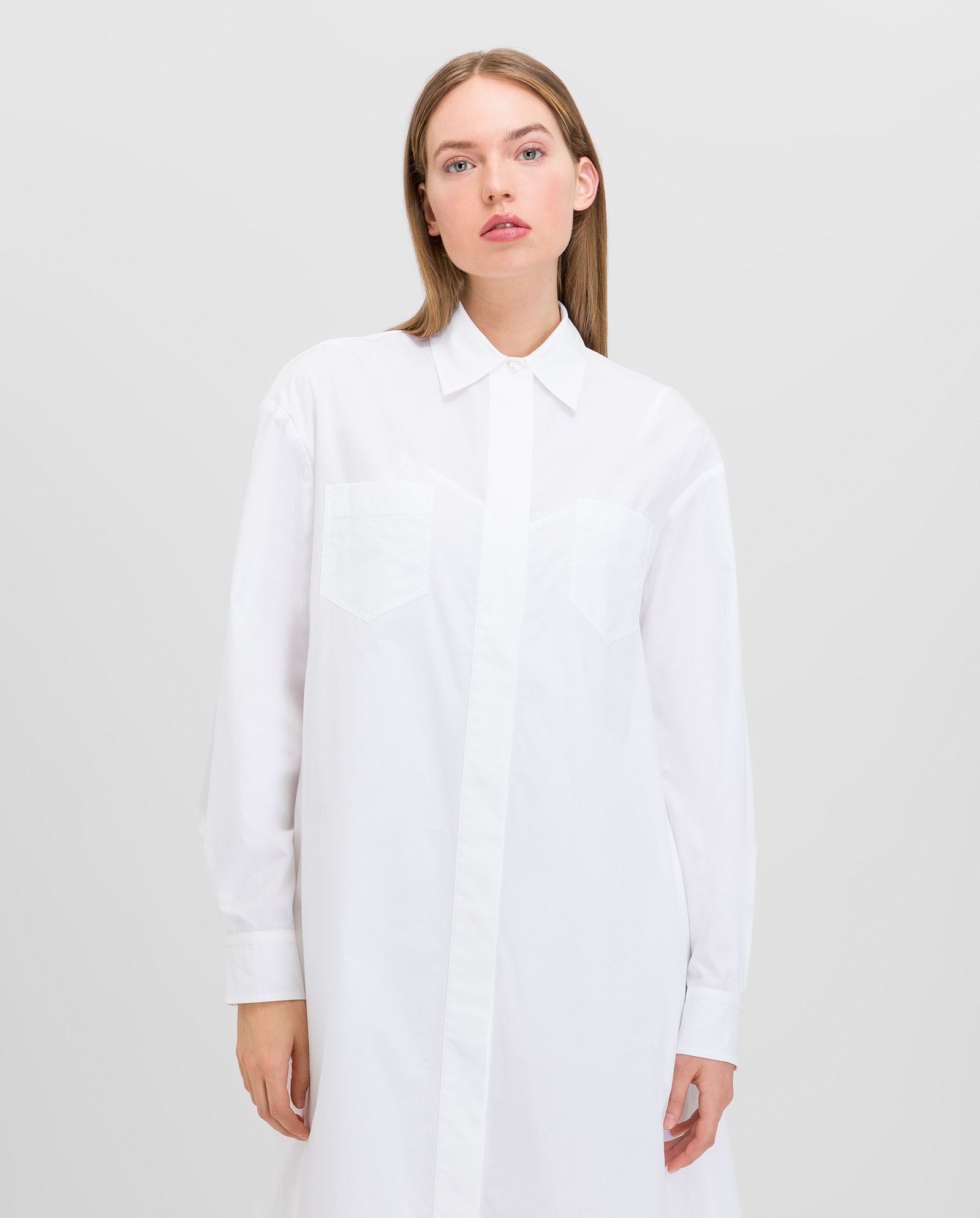 A woman wearing the IVY OAK DINA ANN long-sleeved, ankle-length white dress made from organic fabric, standing against a plain light background.