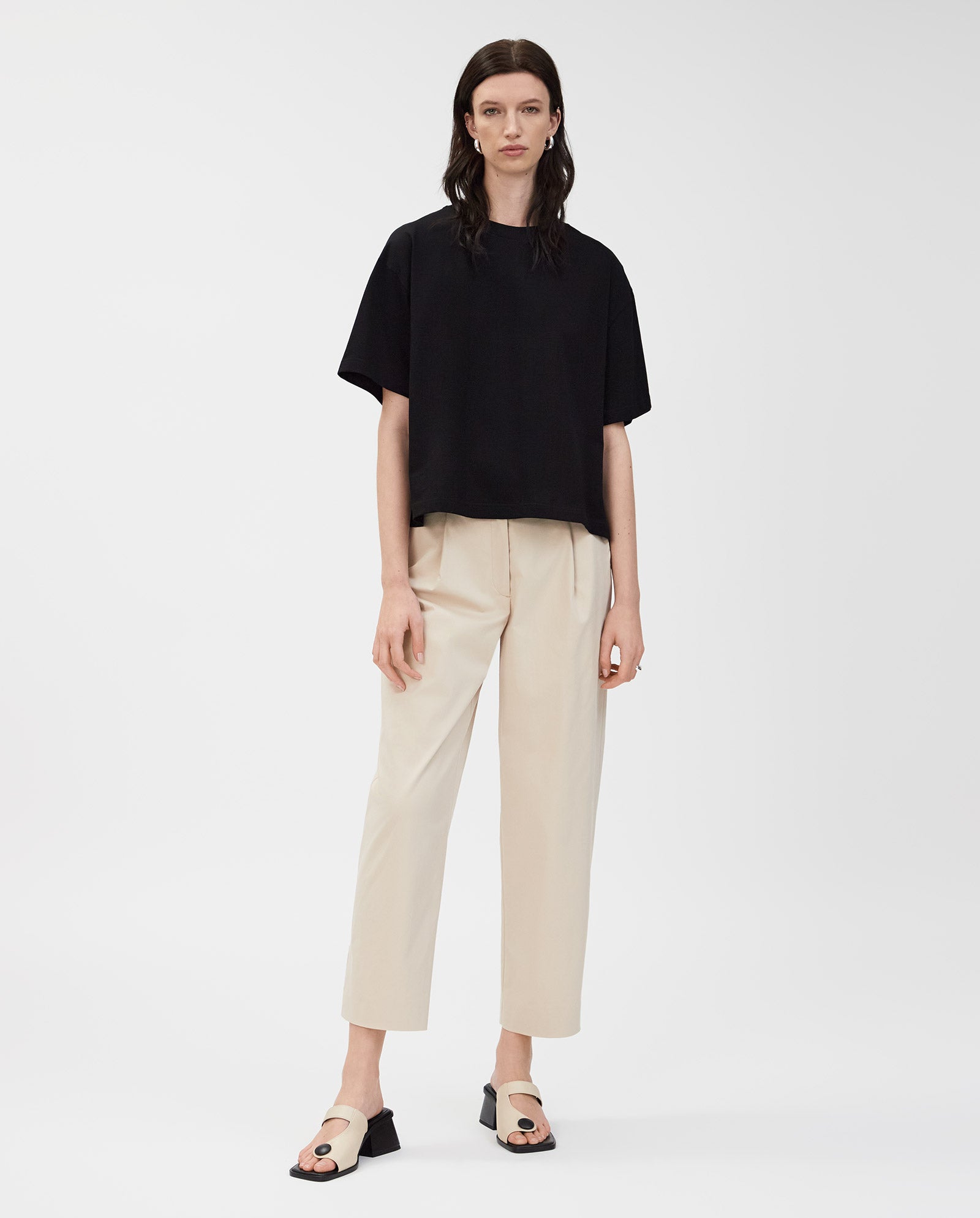 A woman wears the IVY OAK KYLA T-Shirt, styled with beige pants and block heel beige sandals, standing against a white background.