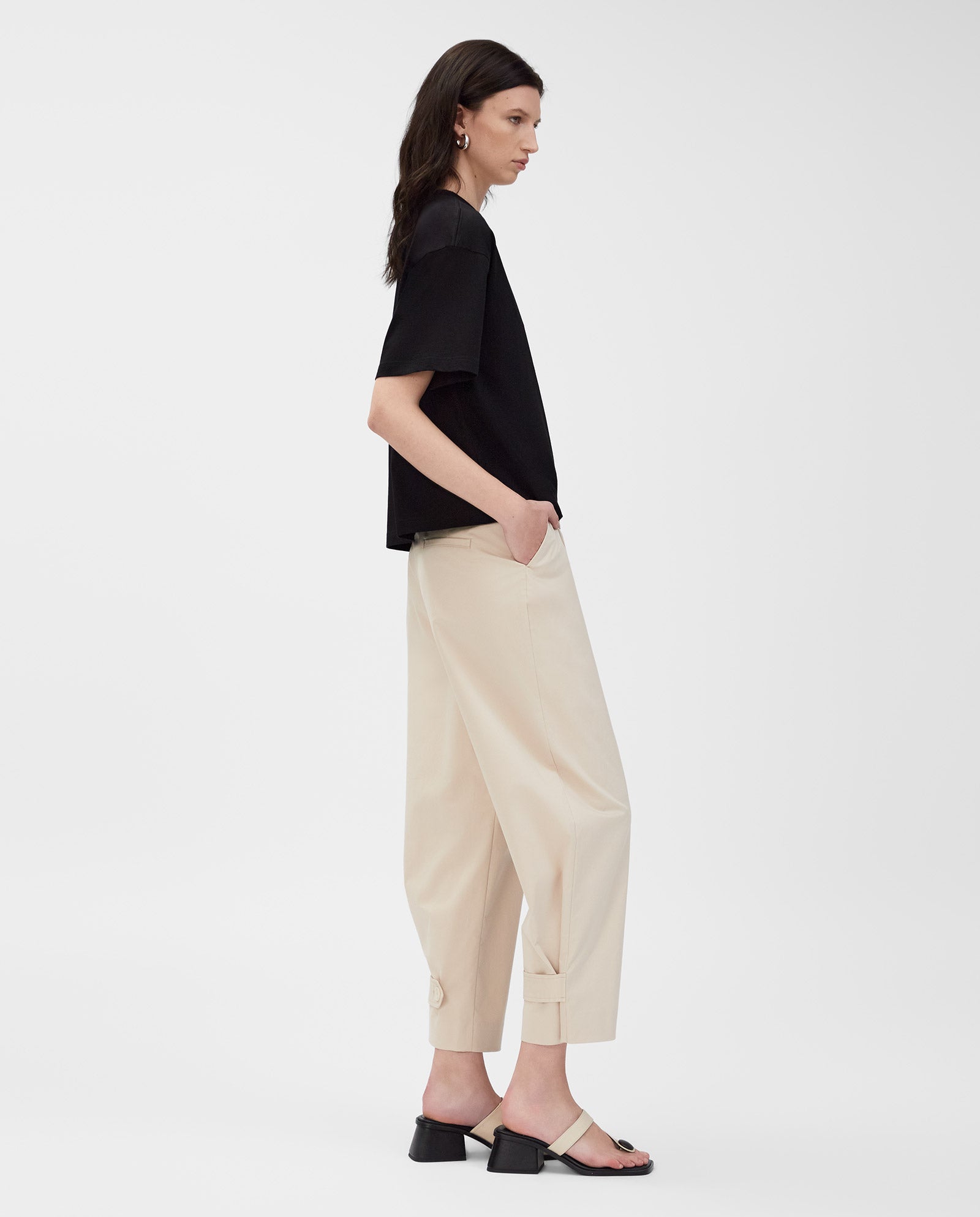 Woman wearing the IVY OAK KYLA T-Shirt in black and beige pants with sandals, standing in profile against a plain white background.