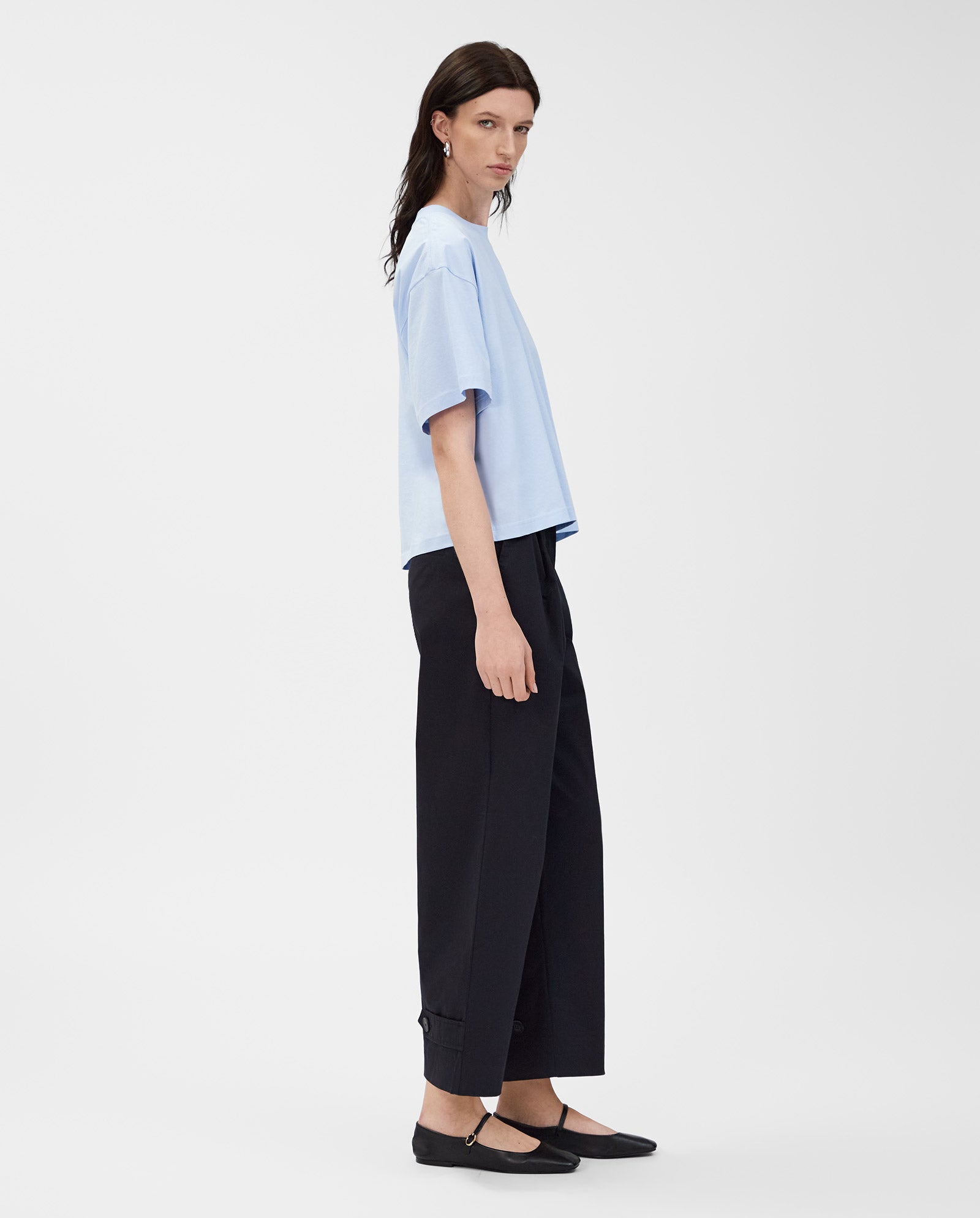 Model wears the essential IVY OAK KYLA T-Shirt in light blue, paired with wide black pants and black flats, standing against a plain white background.
