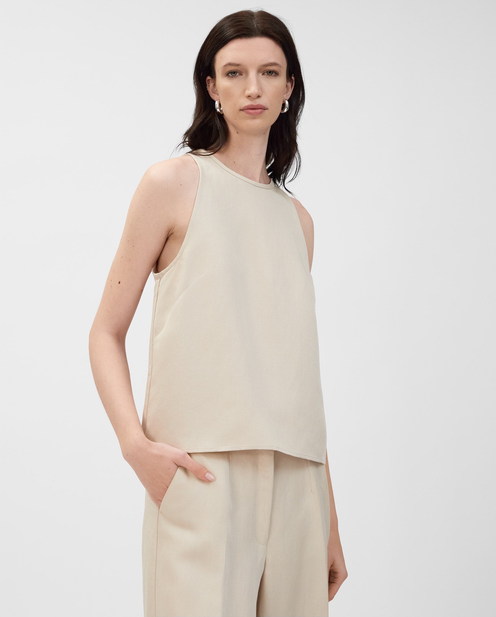 A woman wears the IVY OAK TAILOR SUE sleeveless American shoulder top in beige linen blend with matching pants, one hand in her pocket.