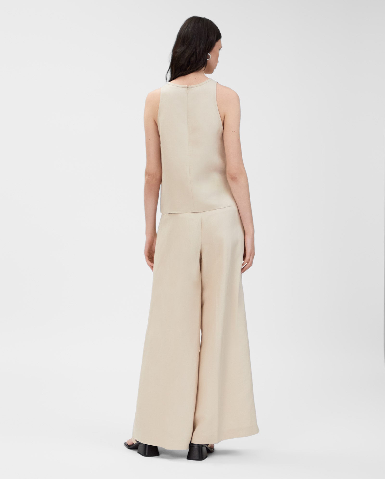 Woman wearing the IVY OAK TAILOR SUE sleeveless beige american shoulder top in a linen blend, paired with wide-leg pants, seen from the back against a white background.