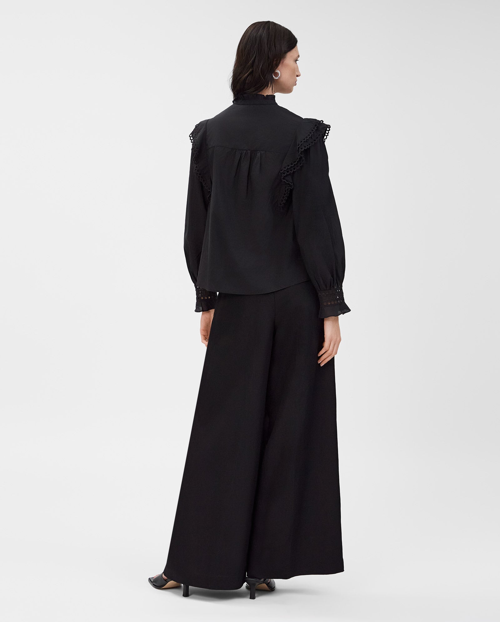 A woman in the IVY OAK EVELINA Blouse, made from cotton voile, pairs it with wide-leg pants and stands with her back to the camera.