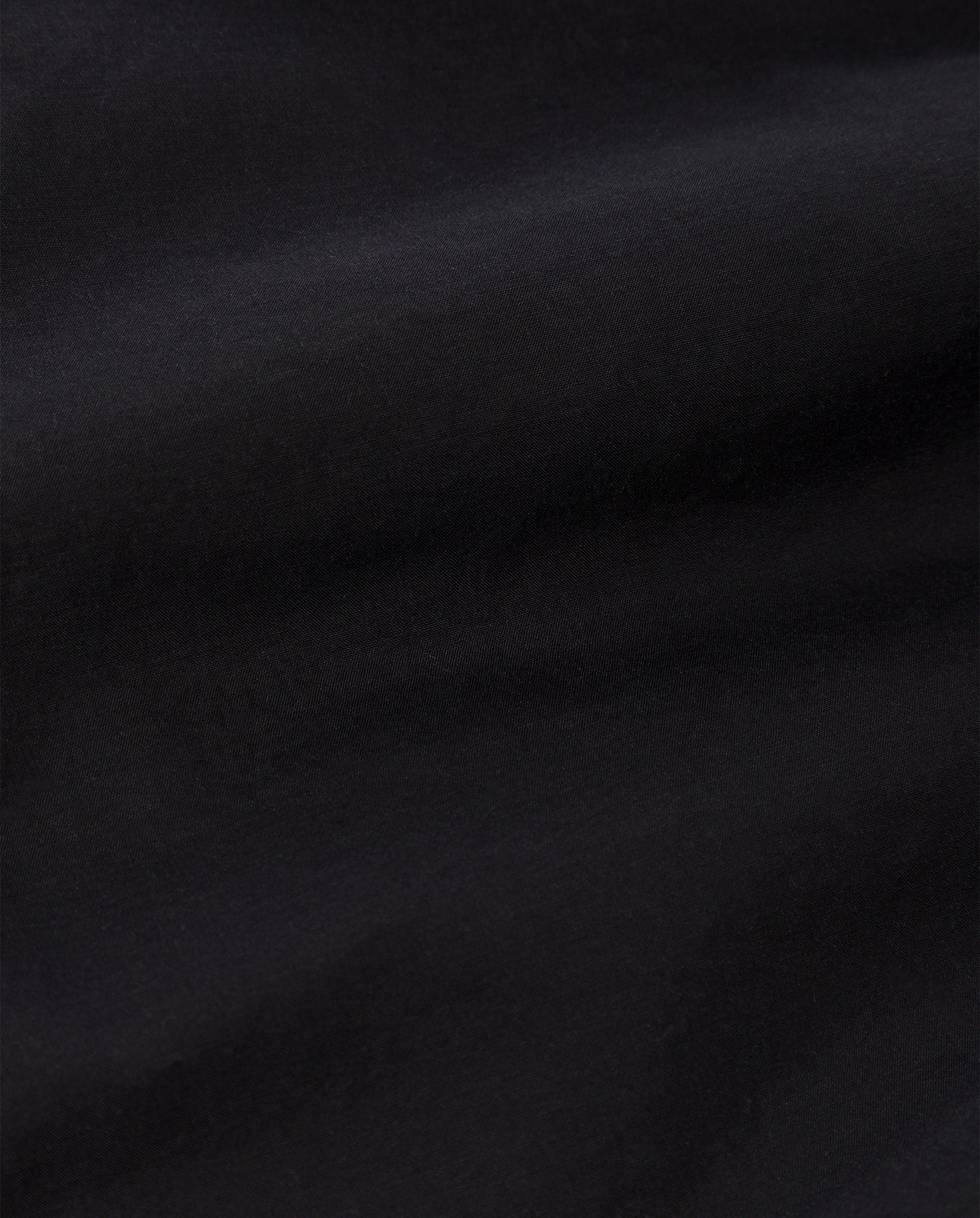 Close-up of the EVELINA Blouse by IVY OAK, showcasing smooth black cotton voile fabric with subtle folds and a soft texture.