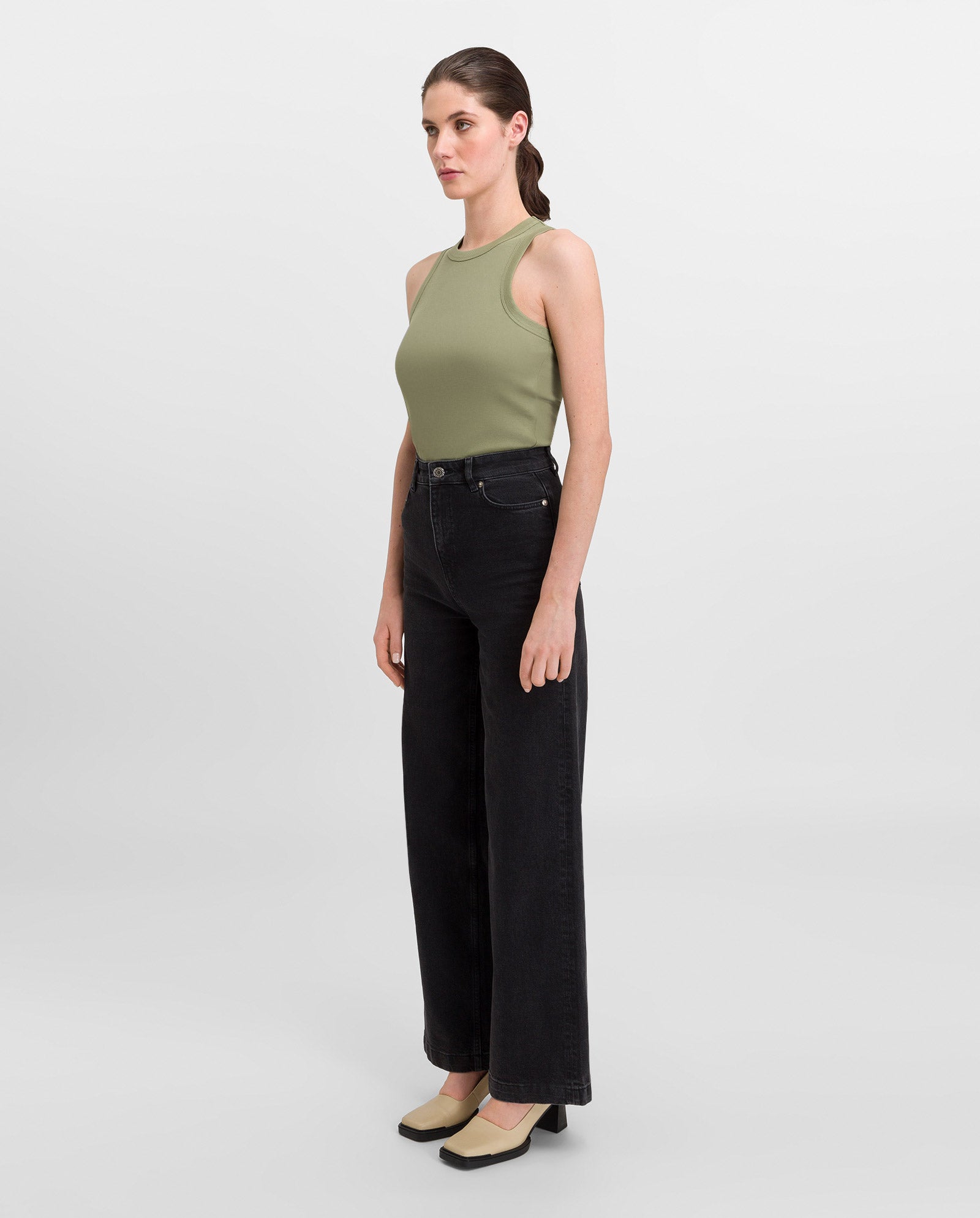 A woman models the IVY OAK KLARA ANN Sleeveless Top in olive green, paired with black wide-leg jeans and beige heels, standing against a gray background.