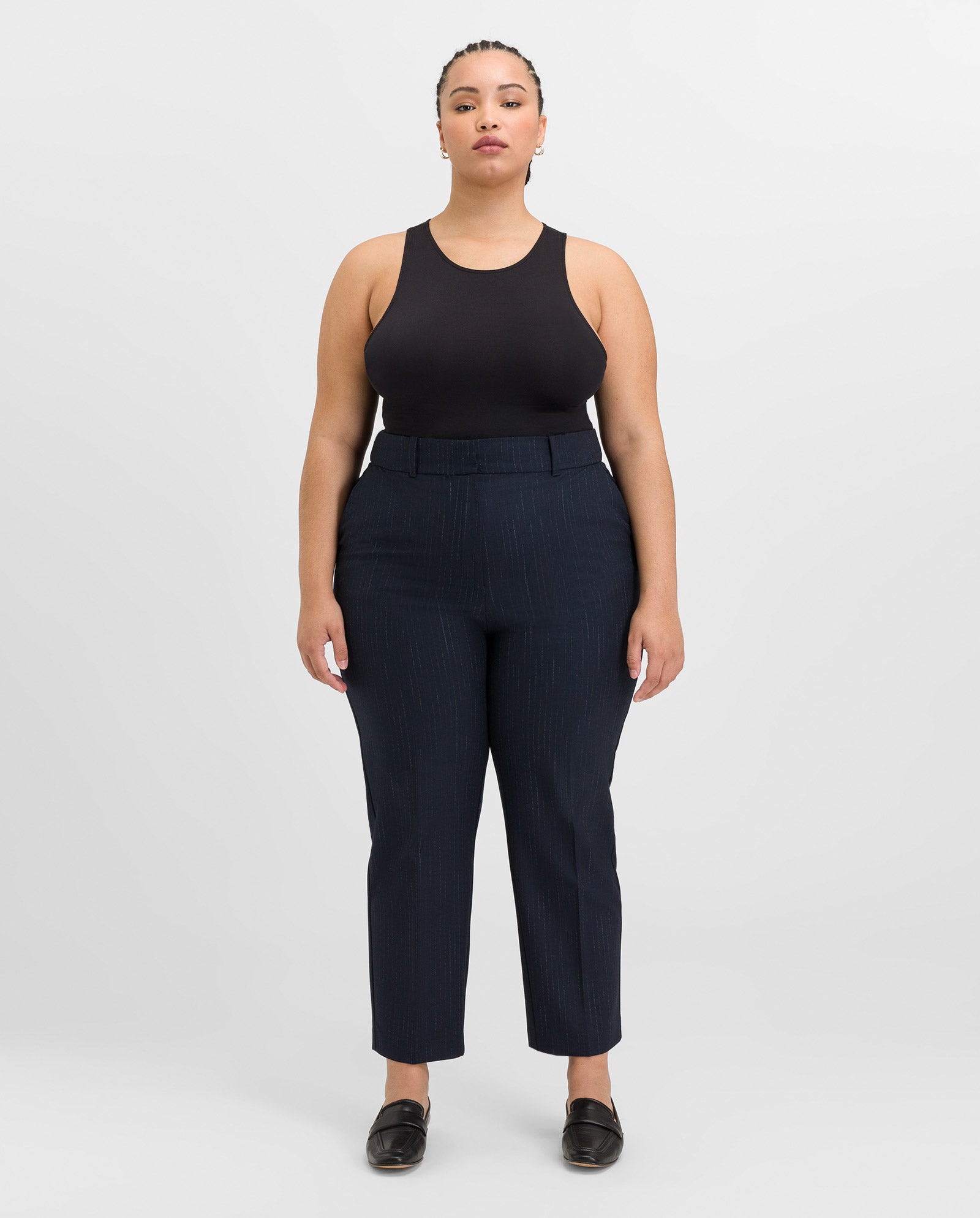 A woman wearing IVY OAK’s PHOEBE ANN Trousers, a black sleeveless top, and black shoes stands facing forward against a white background.