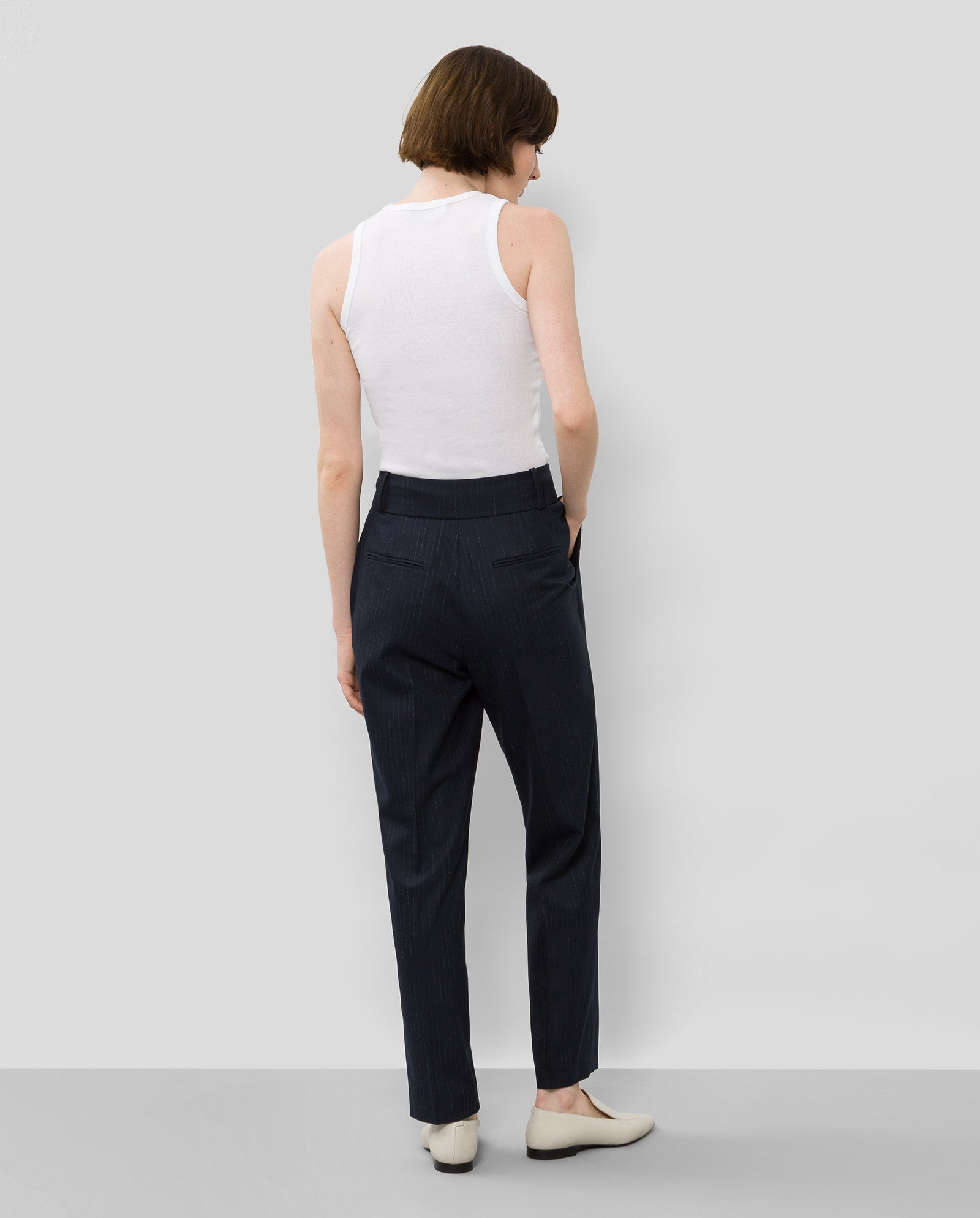 A woman stands with her back to the camera, wearing a white tank top, white shoes, and IVY OAK’s PHOEBE ANN Trouser.