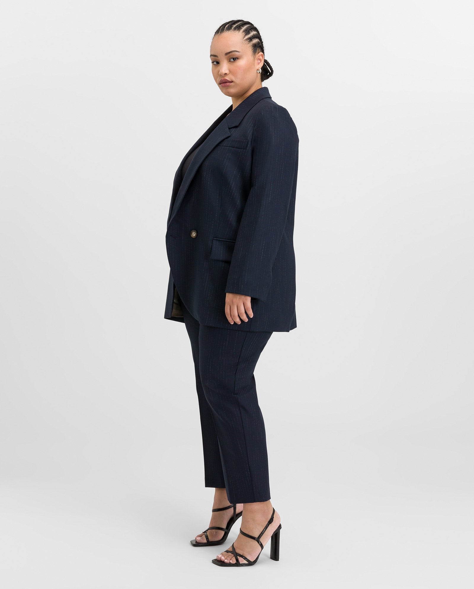 A woman in the IVY OAK JANINA ANN Blazer with piped pockets and black heels stands sideways, looking at the camera against a plain backdrop.