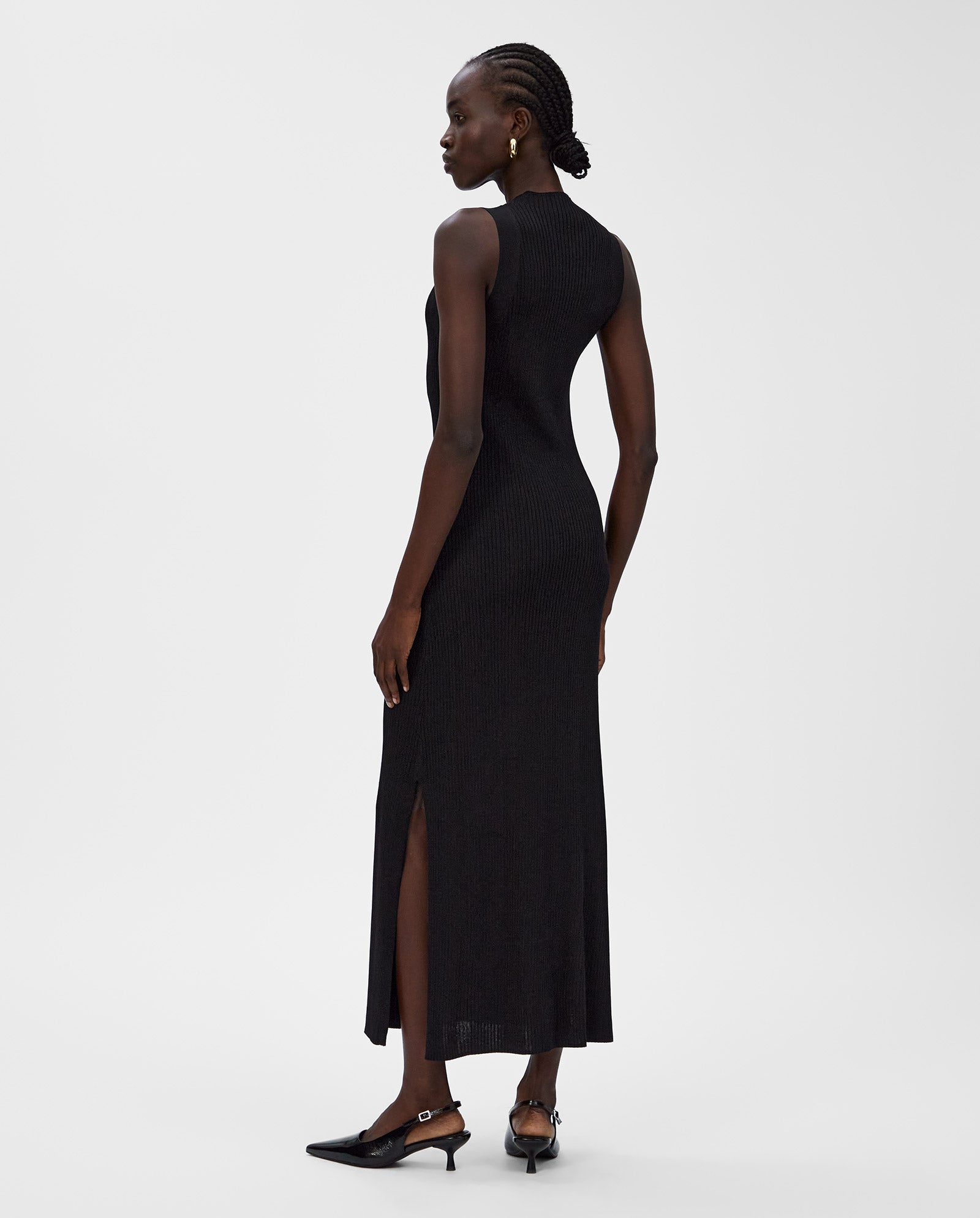 A woman stands facing away from the camera, wearing the IVY OAK KLAUDIA Dress—a sleeveless knit style with rib structure and side slits.
