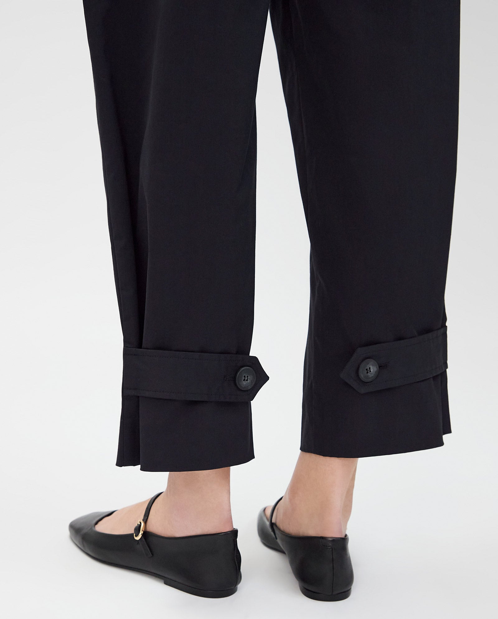 A person wearing IVY OAKs PERSEPHONE Trousers, featuring a high waist and adjustable hem, paired with black flats and shown from the back at ankle level.
