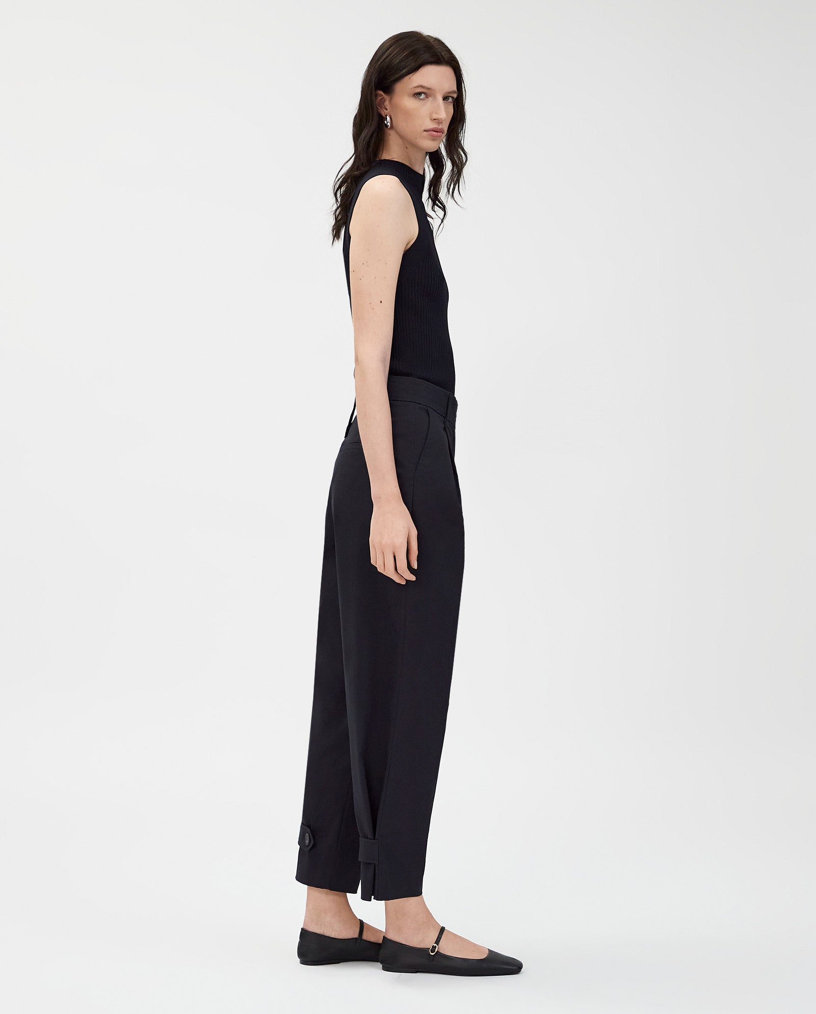 A person wears IVY OAKs PERSEPHONE Trousers with an adjustable hem and a black sleeveless top, paired with black flats, against a plain white background.