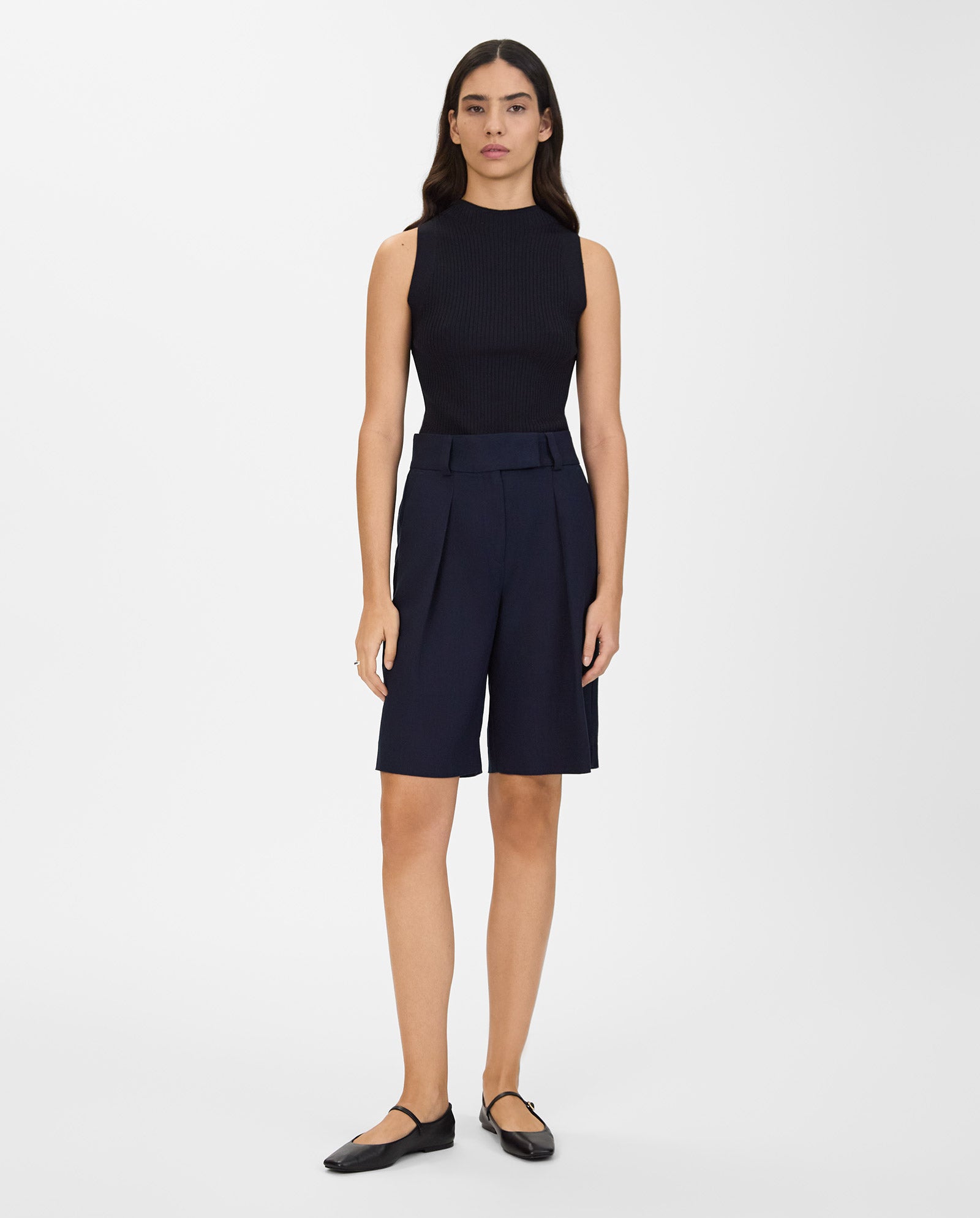 A woman stands against a white background wearing a sleeveless black top, IVY OAK PEONY SUE wide-leg knee-length trousers with subtle pleats, and black flats.