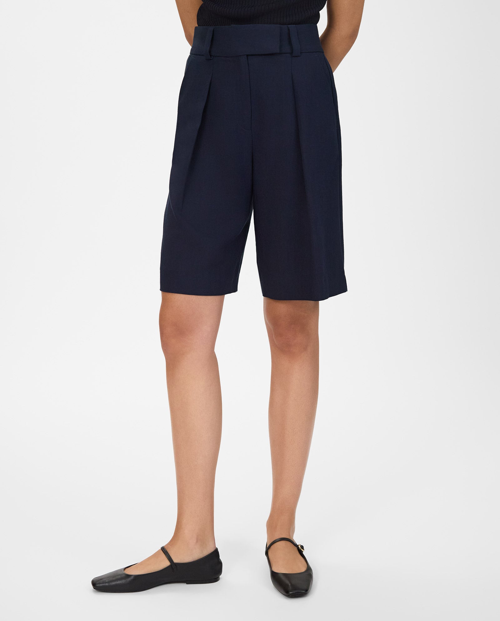 Person wearing navy PEONY SUE Trousers by IVY OAK with pleats and a wide leg, paired with a black top and black ballet flats on a white background.