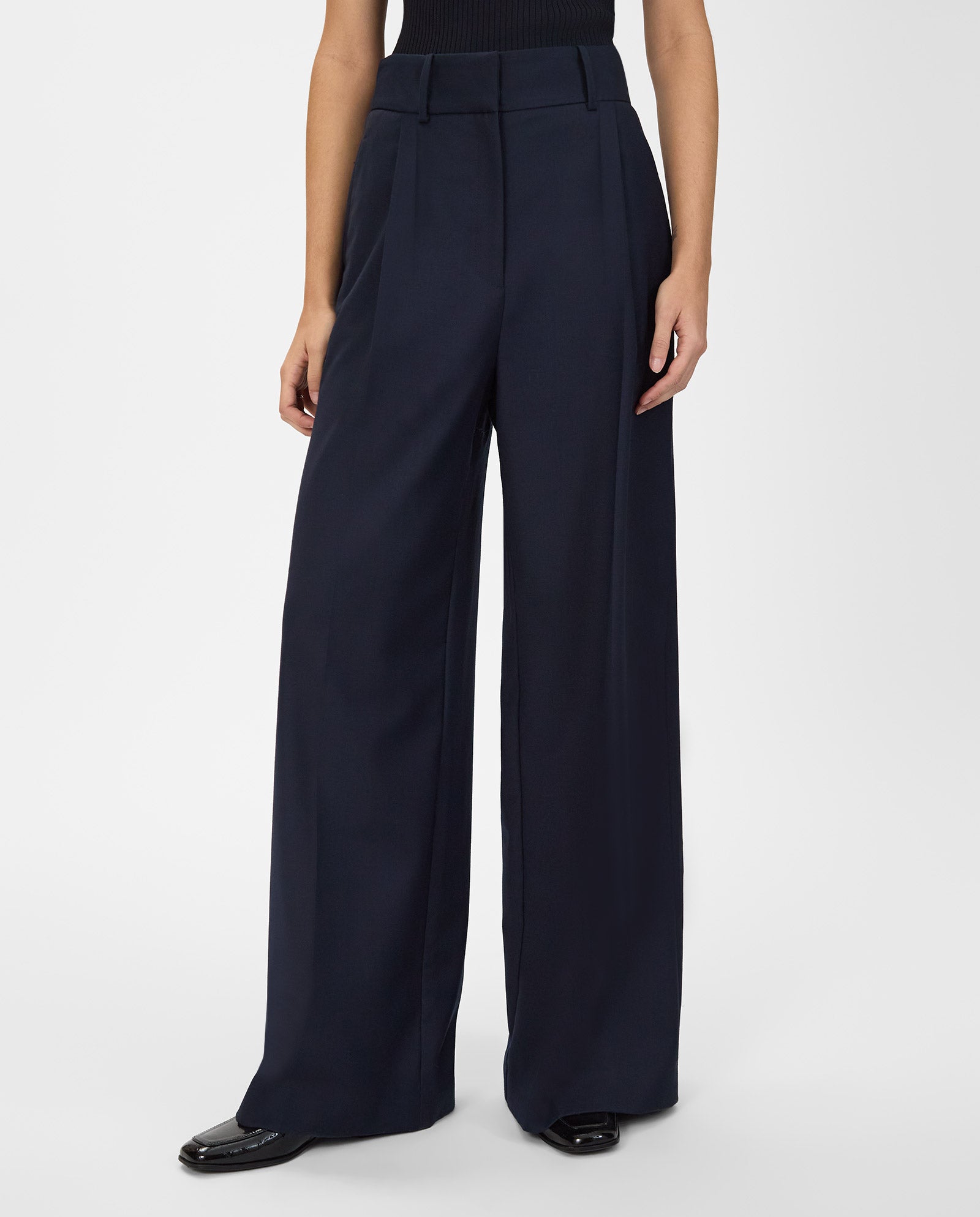 Person wearing IVY OAK PRESCILLIA ANN Pants, high-waisted and wide leg in navy, paired with black shoes and a sleeveless black top.