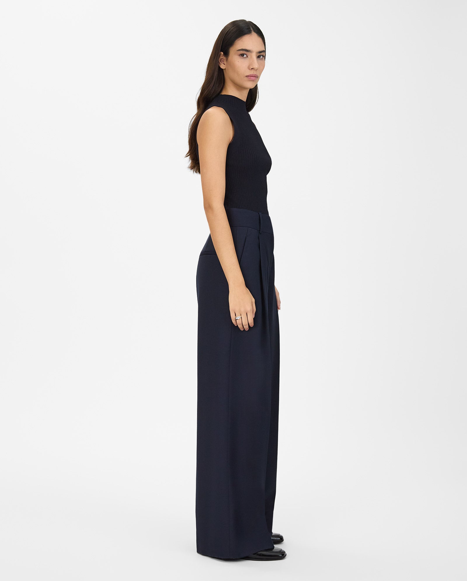 A woman models the IVY OAK PRESCILLIA ANN Pants, styled with a sleeveless black top, standing sideways against a white background.