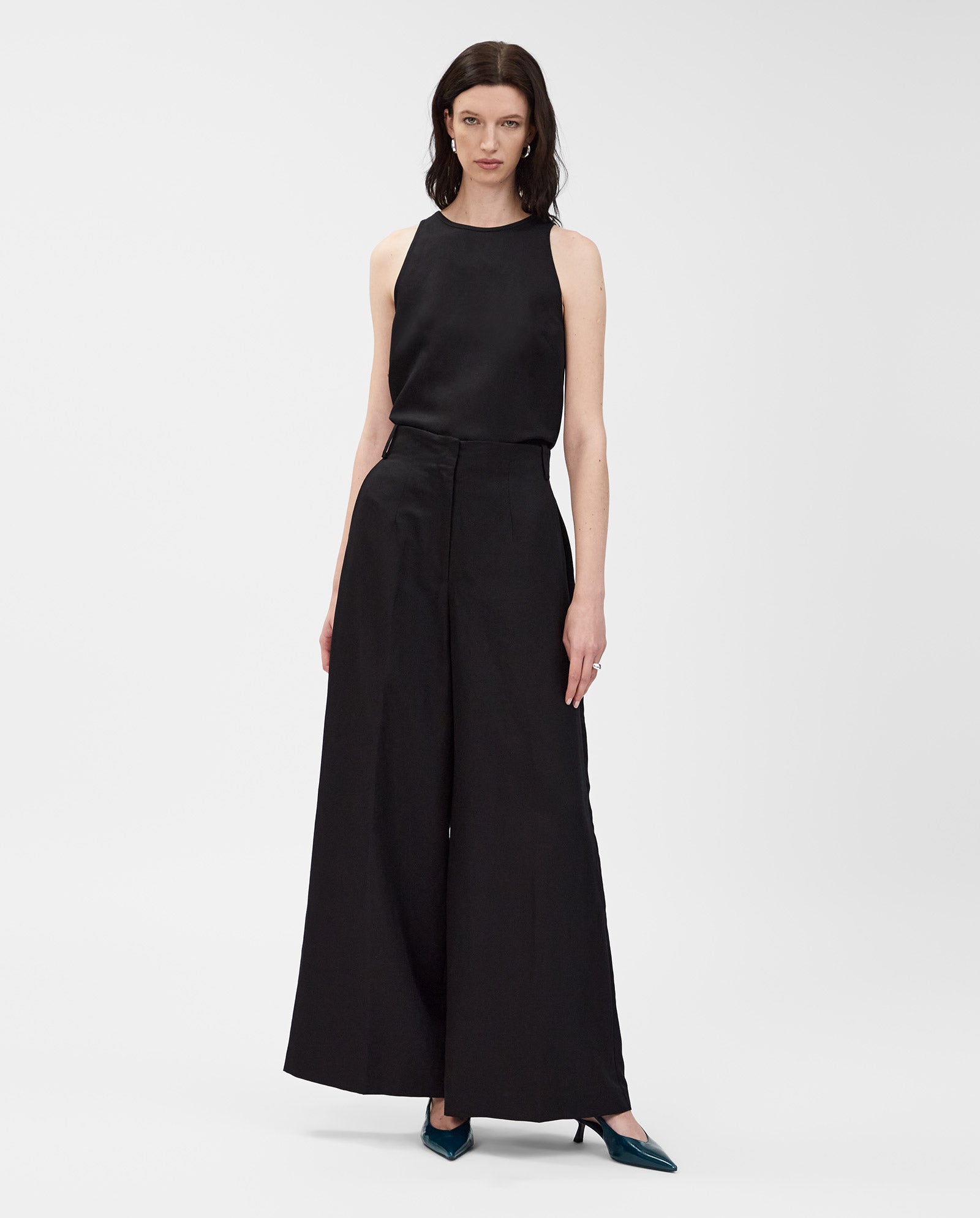 Woman in sleeveless black top and IVY OAK PIERA high waist wide leg trousers, made from a linen blend, paired with teal heels against a white background.