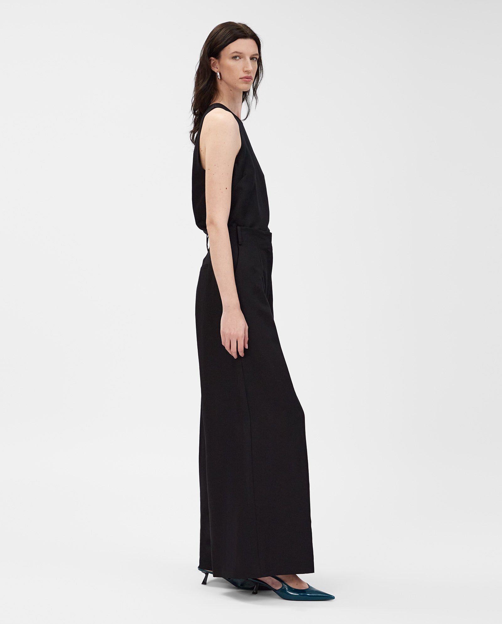 Woman wearing IVY OAK PIERA wide-leg black trousers and teal heels stands sideways against a plain white background.